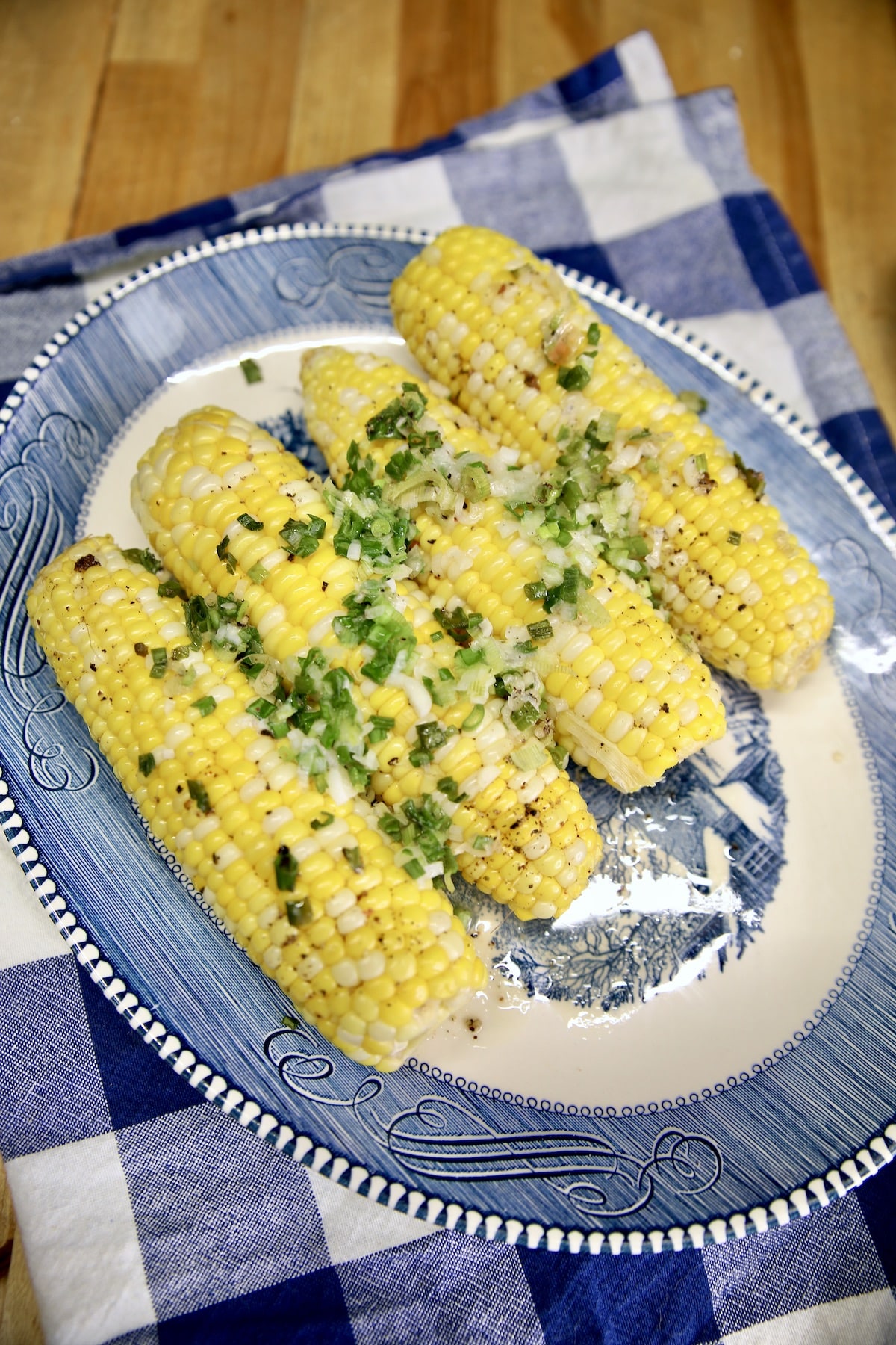 4 ears of corn on a platter with butter and green onions.