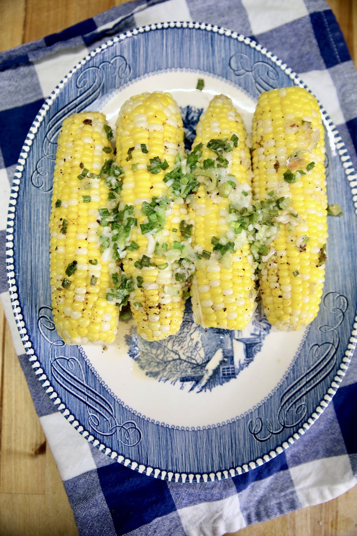 Platter with 4 corn on the cob cooked with green onions and butter.