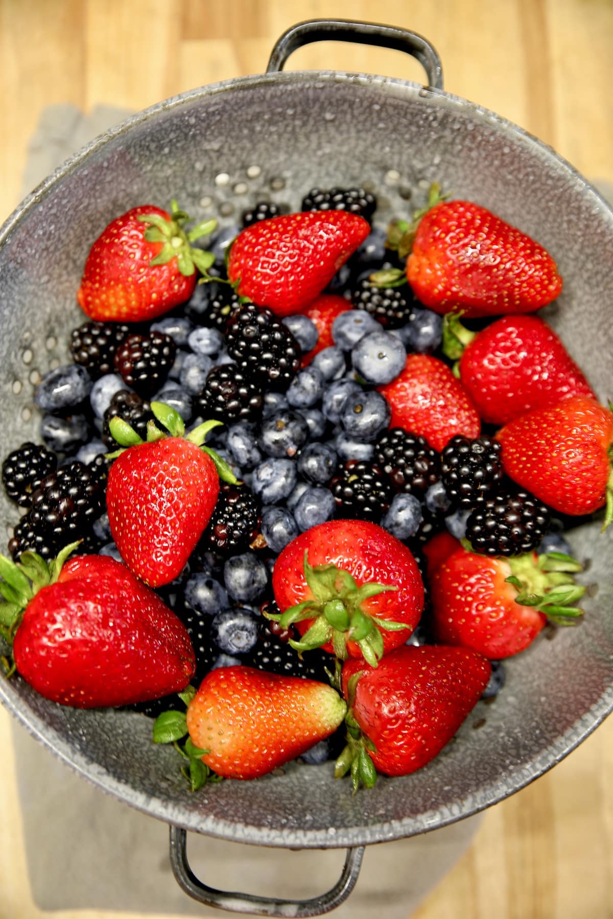 Colander with fresh strawberries, blueberries and blackberries.
