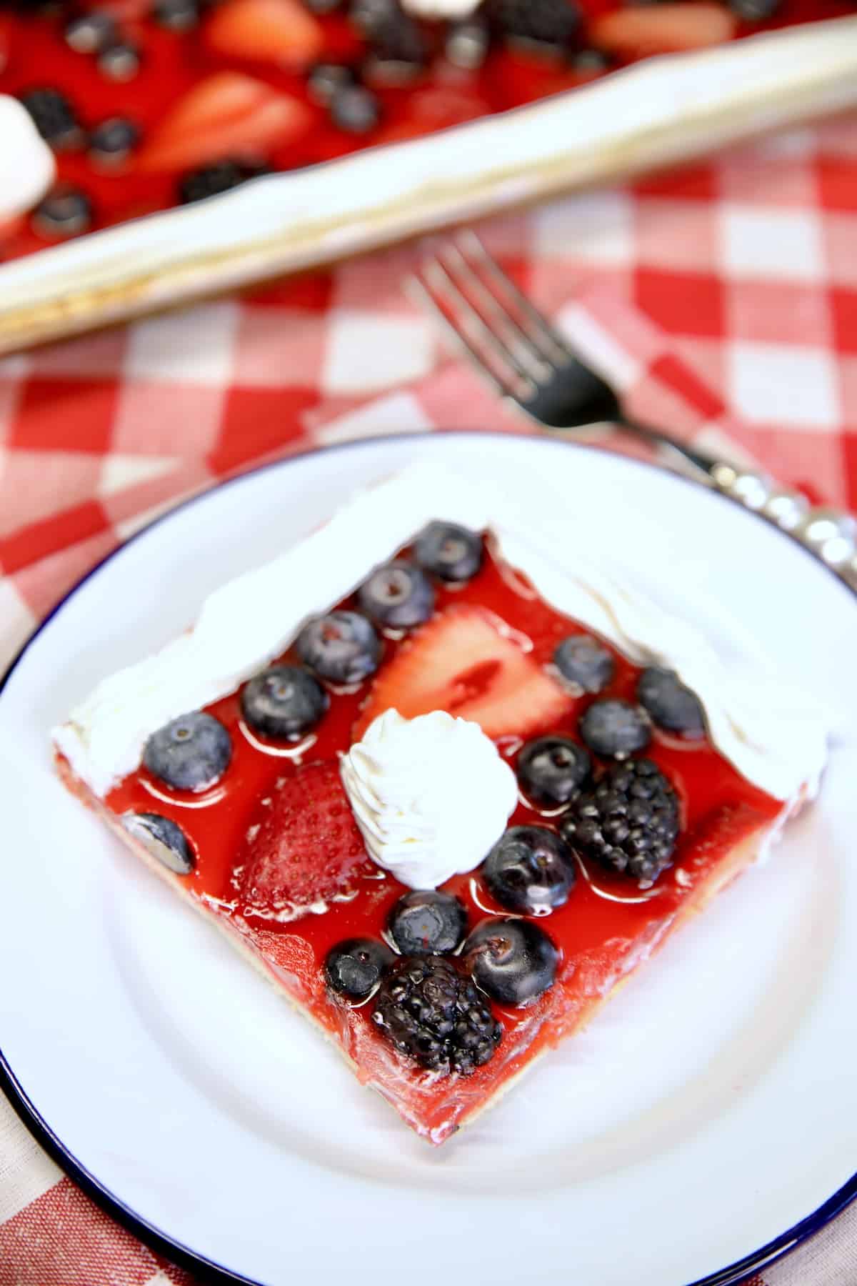 Slice of mixed berry pie with cool whip garnish.