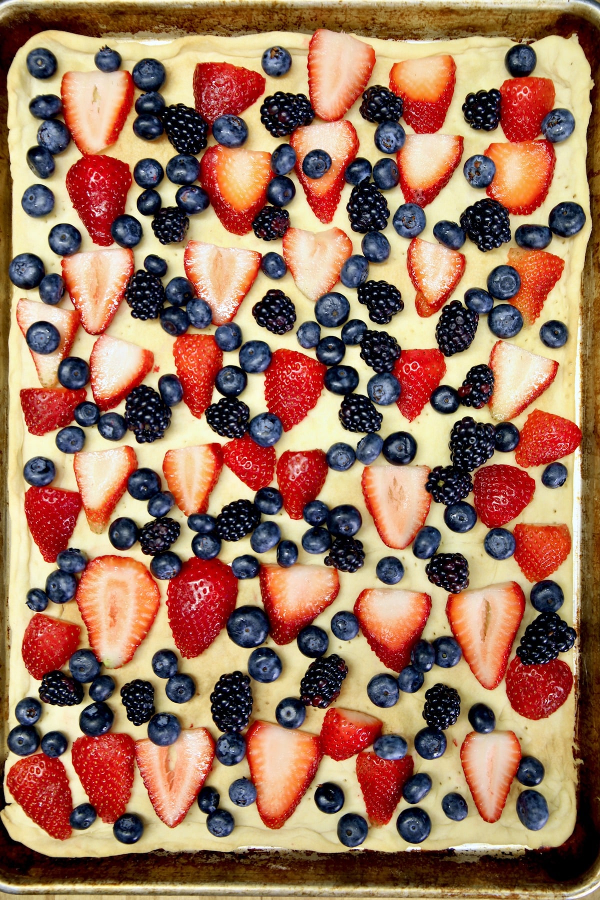 Mixed berries scattered over pie crust in a sheet pan.