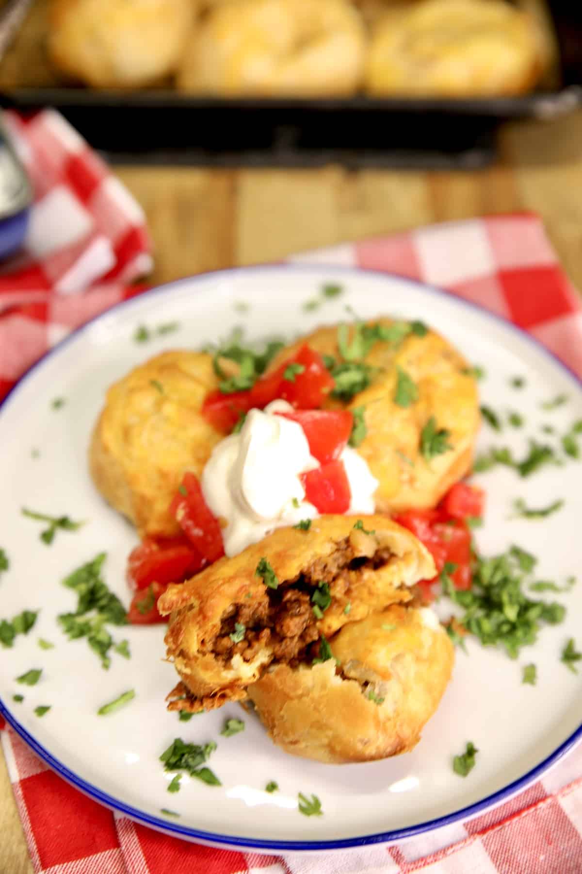 Cheesy Biscuit taco bombs on a plate with sour cream and tomatoes.