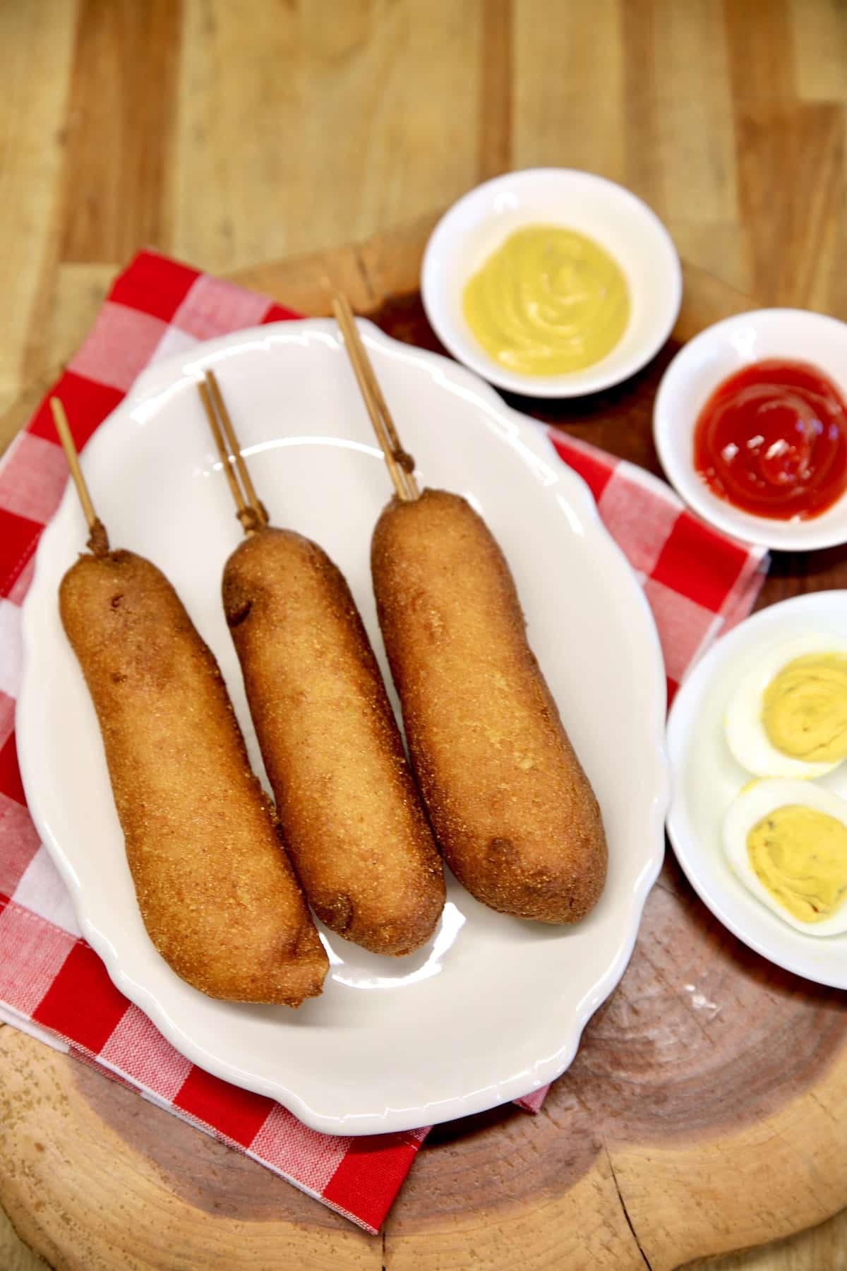Corn dogs on a platter with bowls of mustard and ketchup.