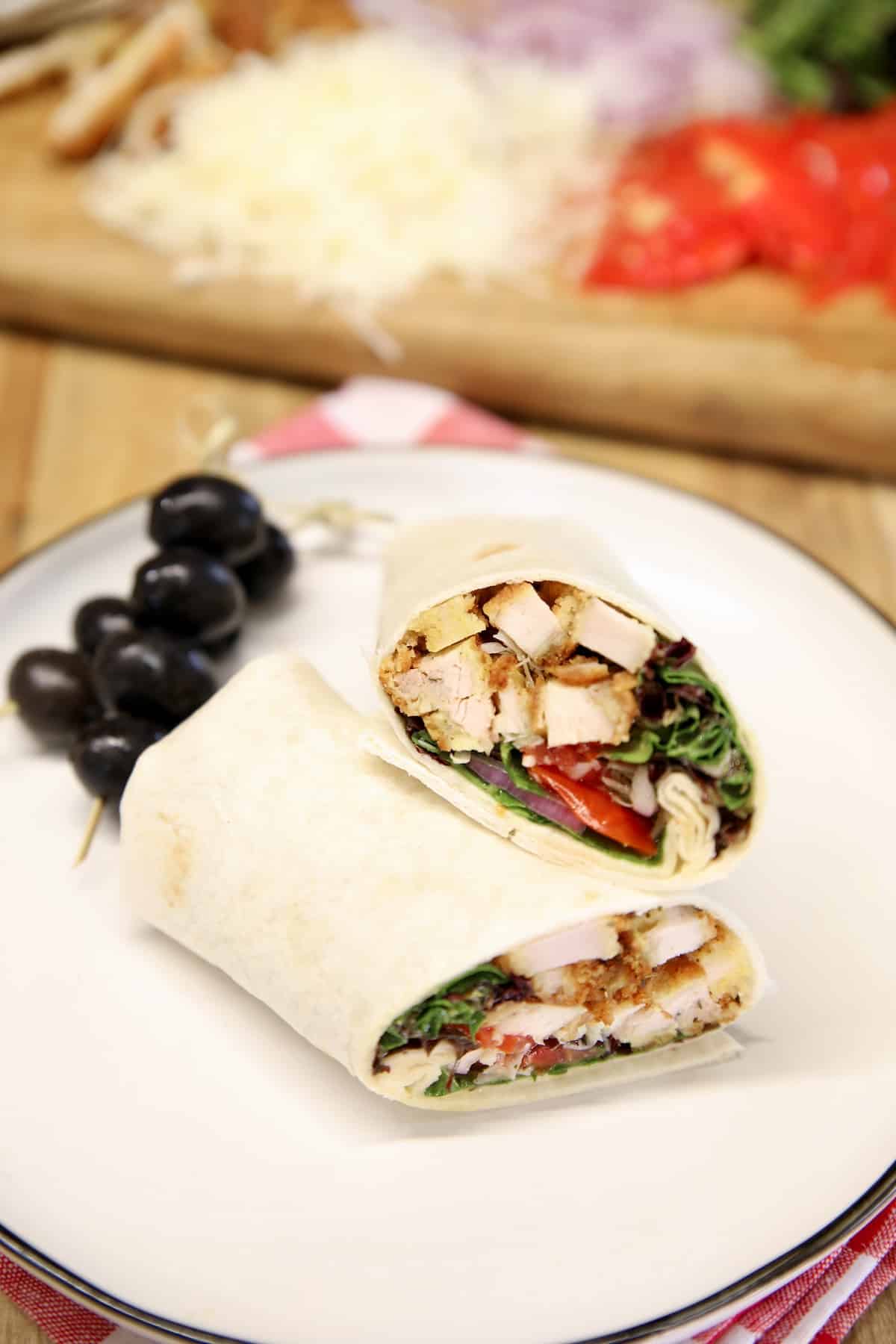 Chicken parmesan wrap cut in half on a plate with olives.