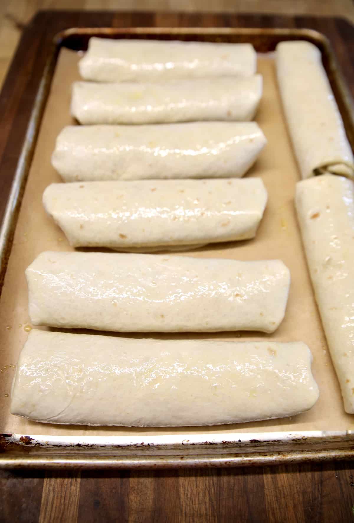 Sheet pan of burritos brushed with olive oil.