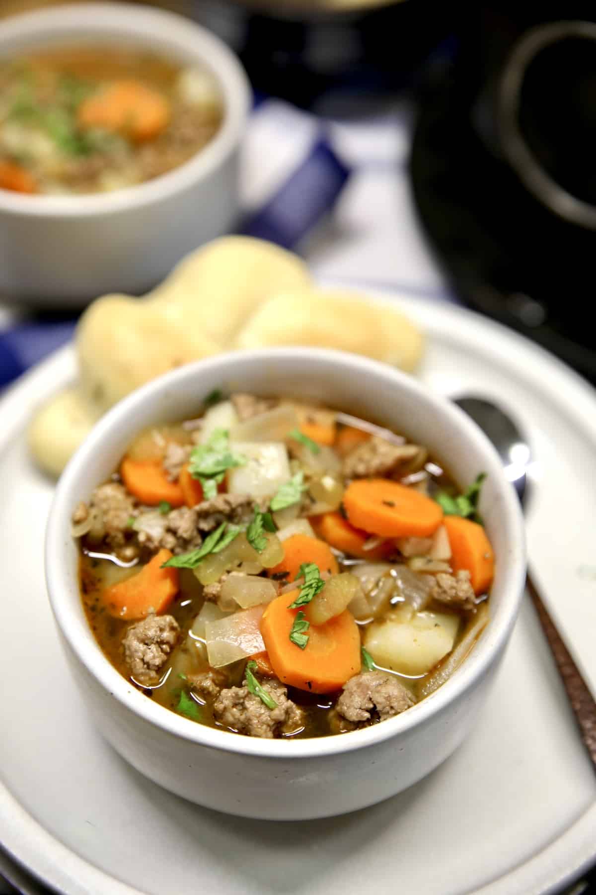 Bowl of beef vegetable soup on a plate with spoon.