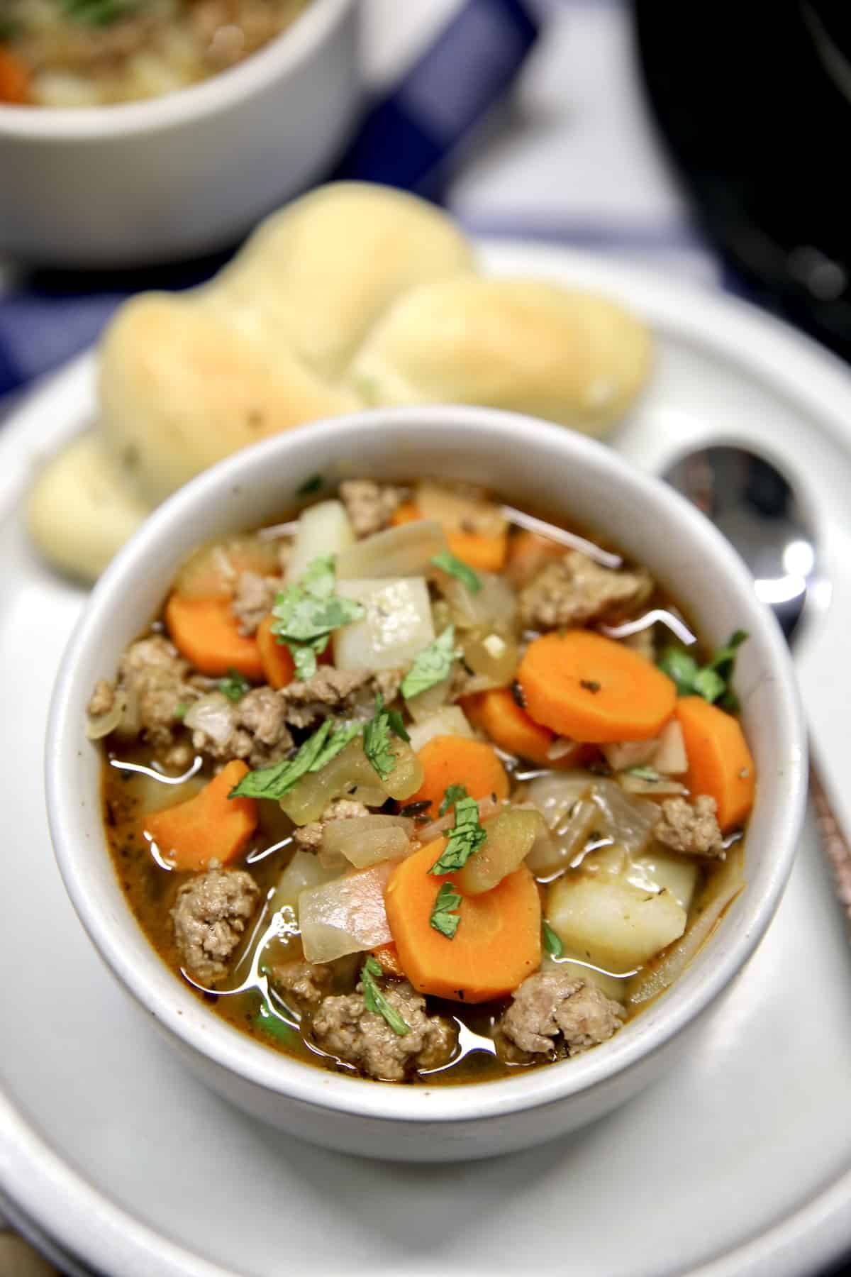 Bowl of ground beef vegetable soup on a plate with a roll.