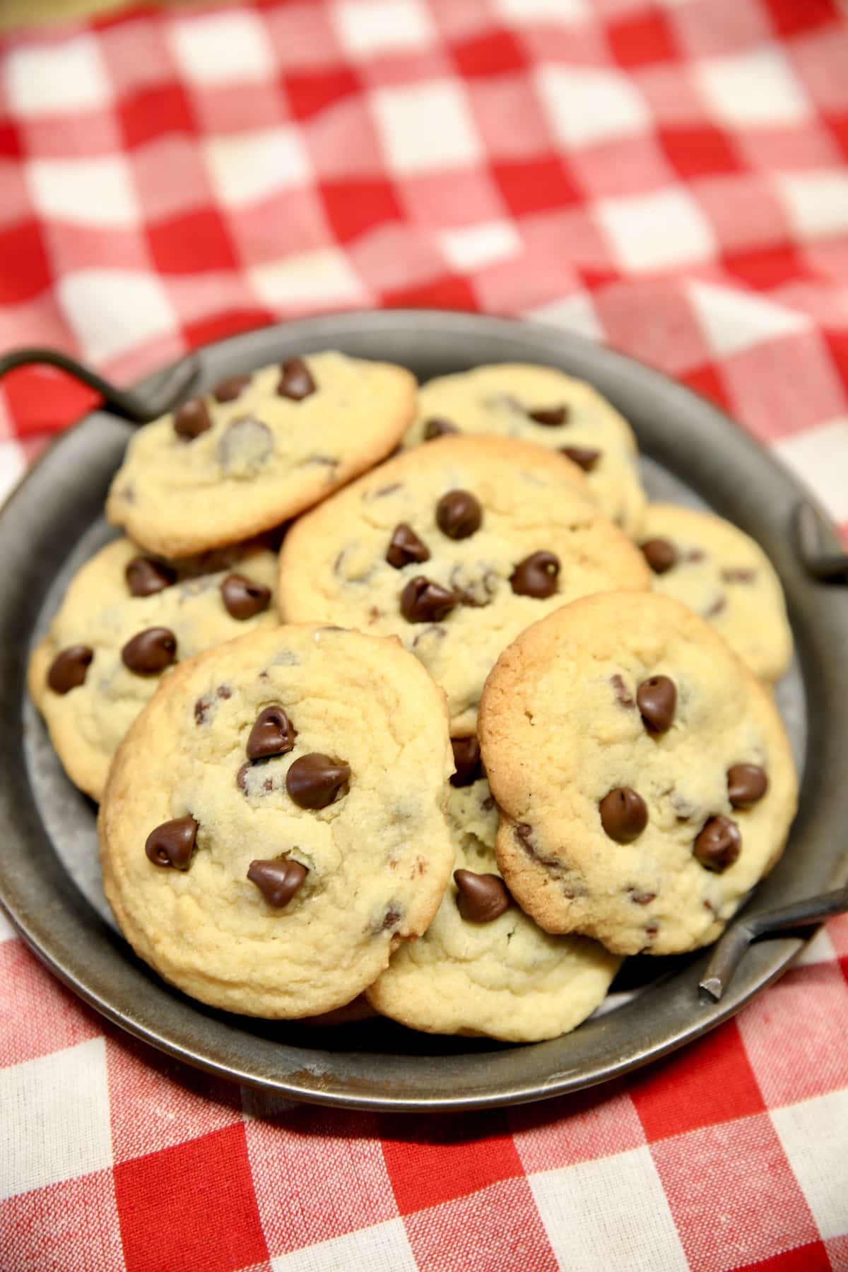Plate of chocolate chip cookies on a red check napkin.