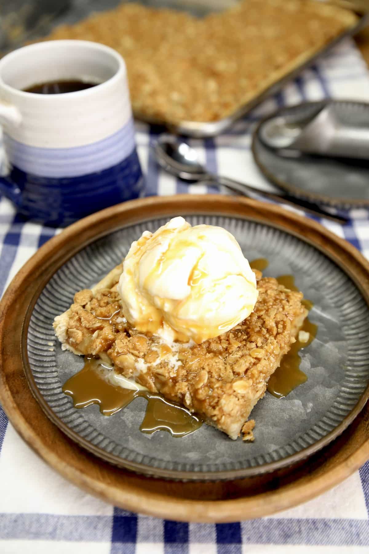 Slice of apple slab pie with ice cream and caramel drizzle, cup of coffee. 