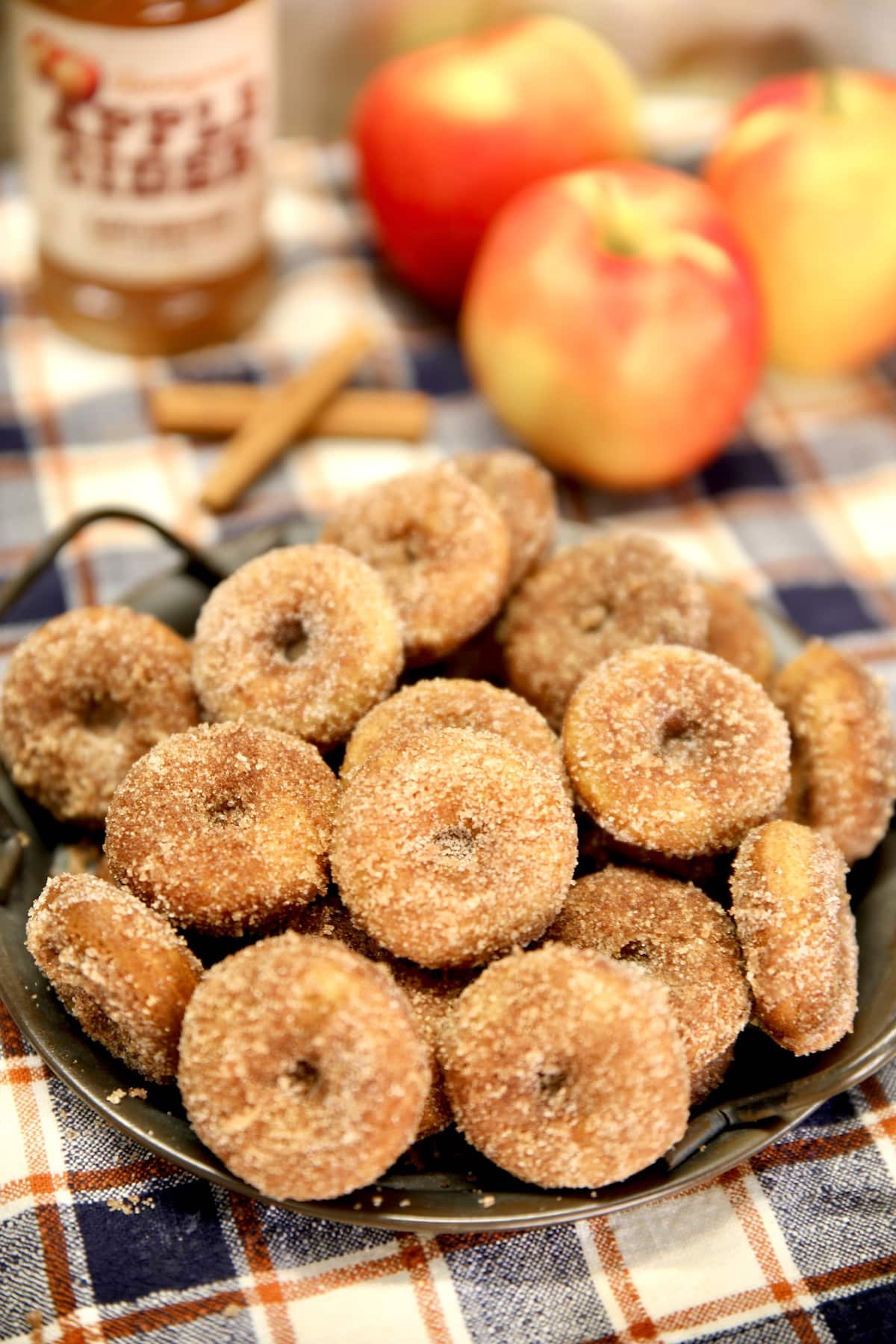Apple cider donuts on a platter, apples and cider in background.