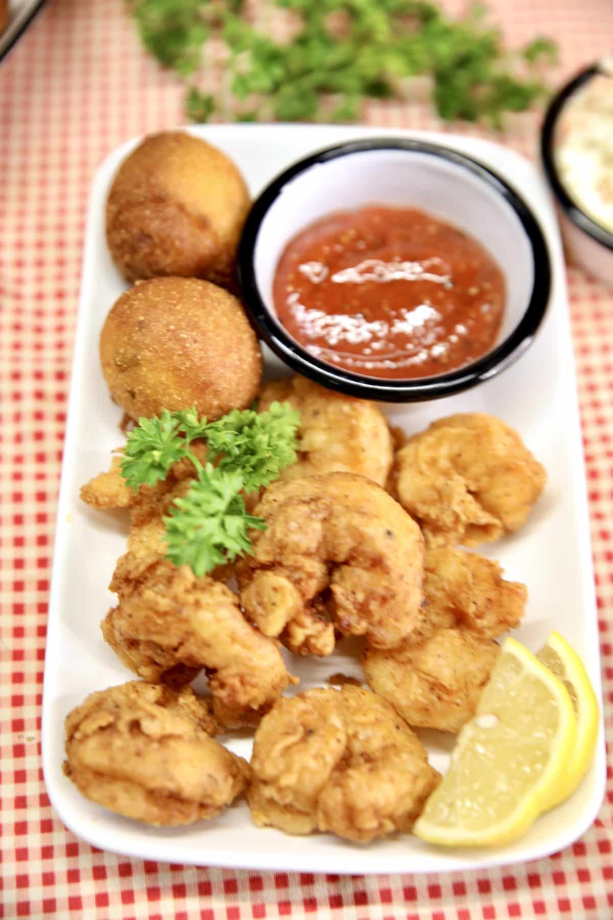 Platter of shrimp and hush puppies with lemon slices and cocktail sauce.
