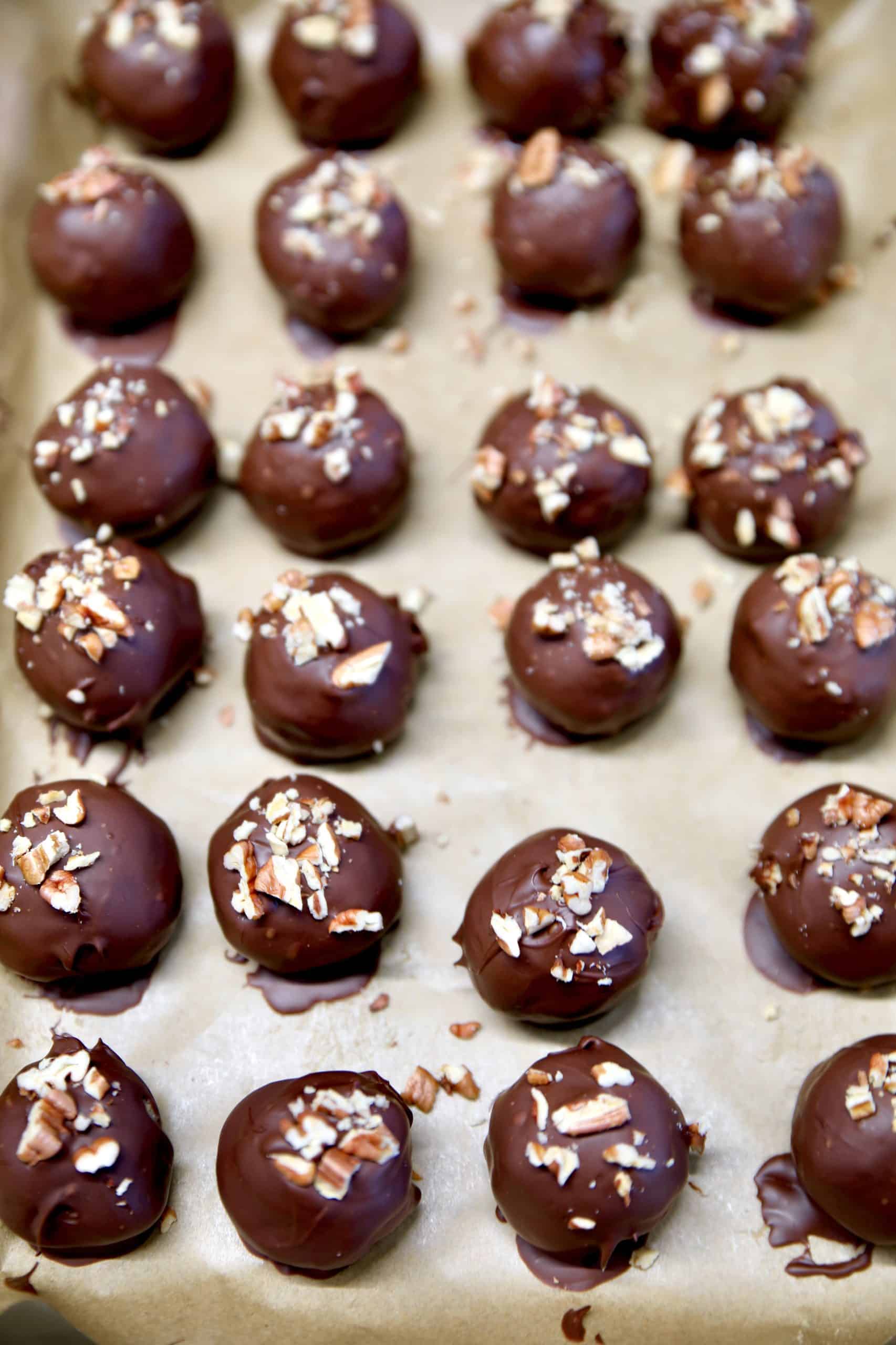 Bourbon pecan balls dipped into chocolate on a cookie sheet.