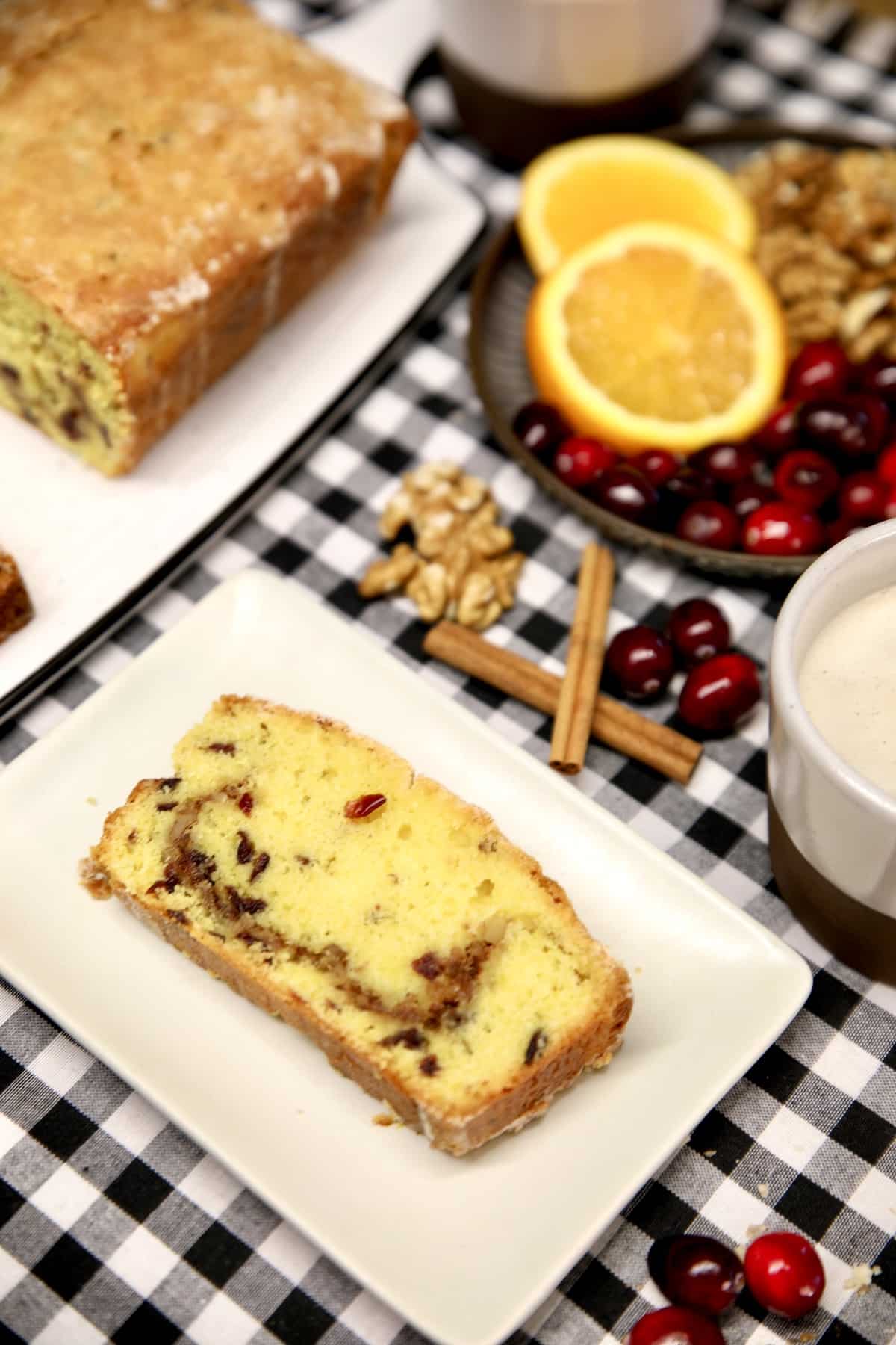 Slice of cranberry cake on a plate, loaf in background.