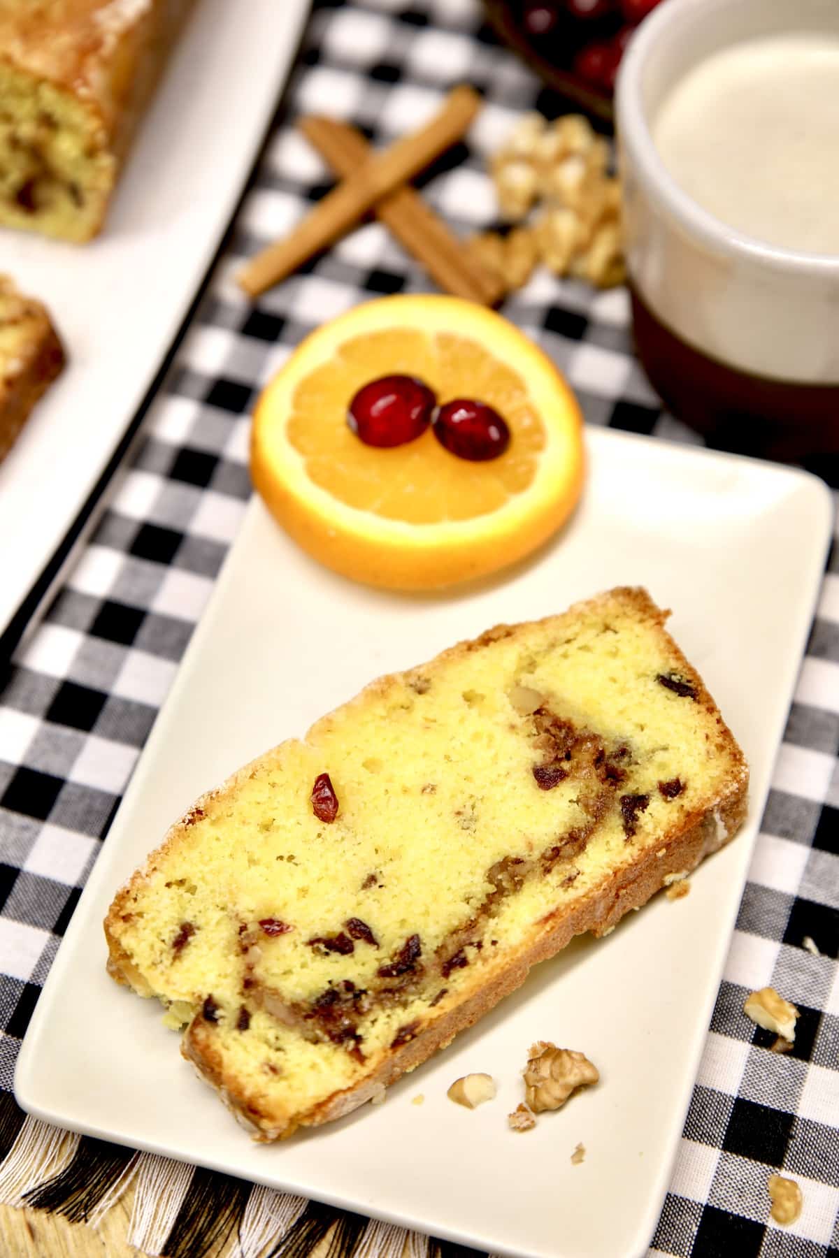 Plate with slice of cranberry cake, orange slices and fresh cranberries.