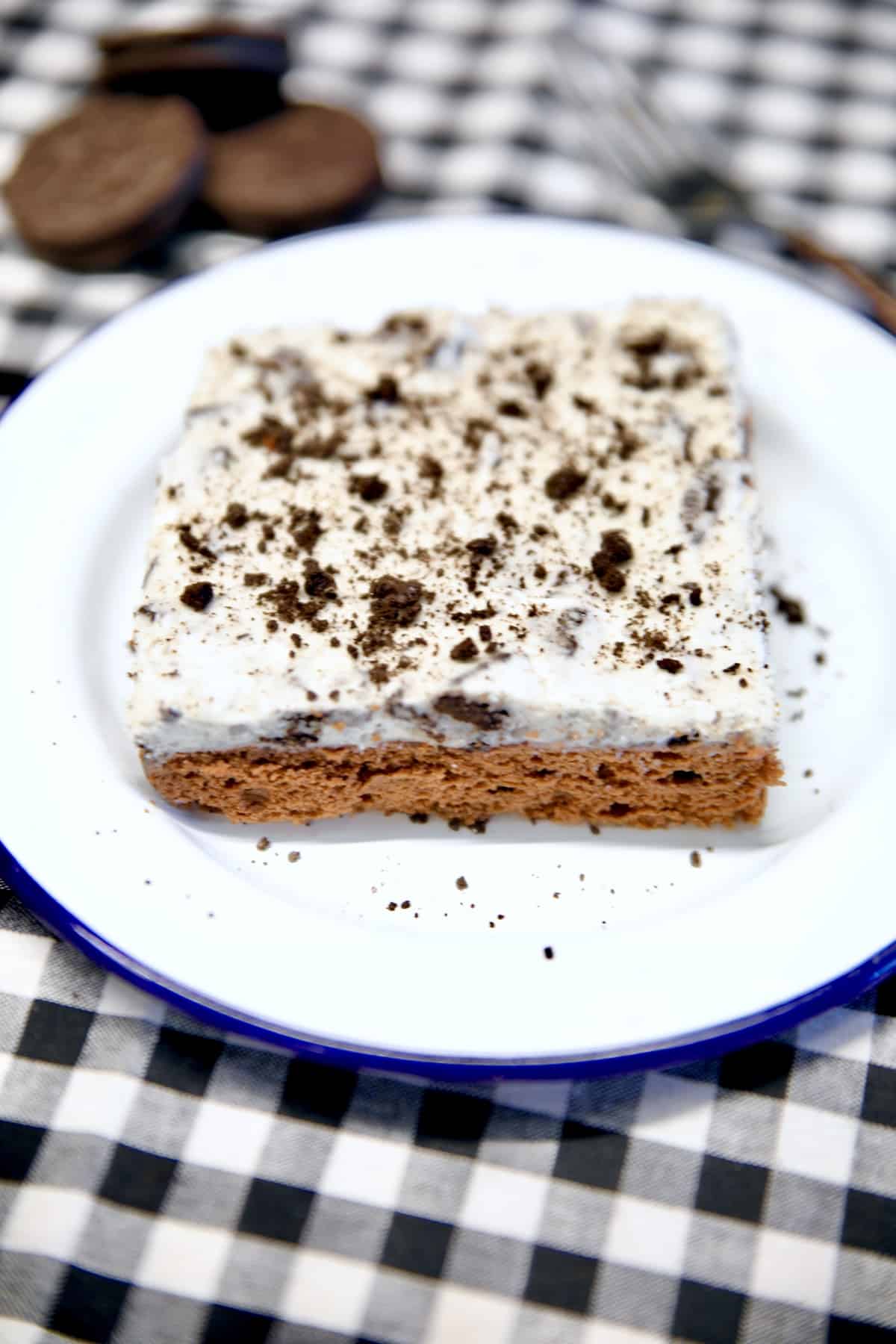 Slice of chocolate cake with cookies and cream icing on a plate.