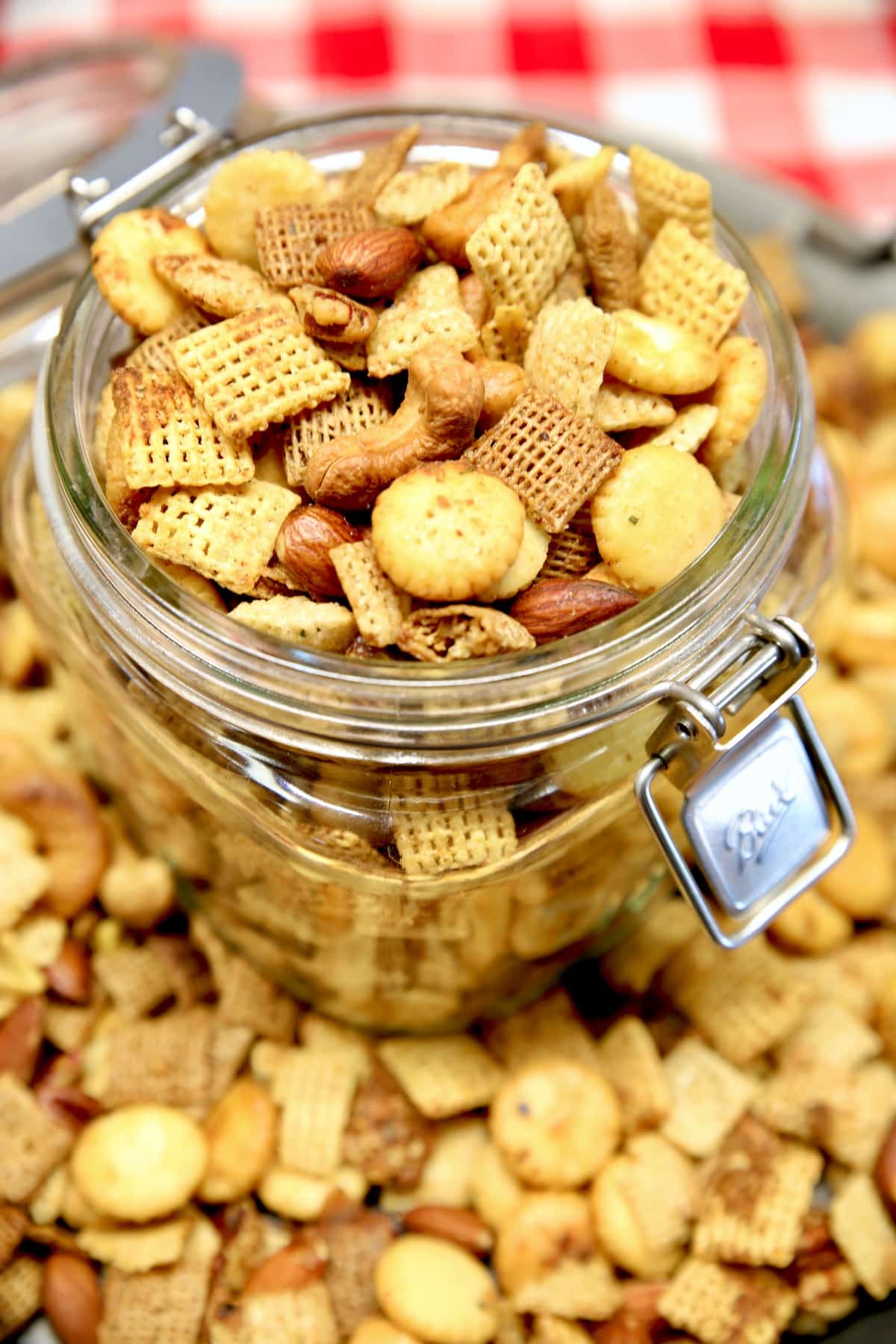 Spicy chex mix in a jar with chex mix on a platter around the jar.