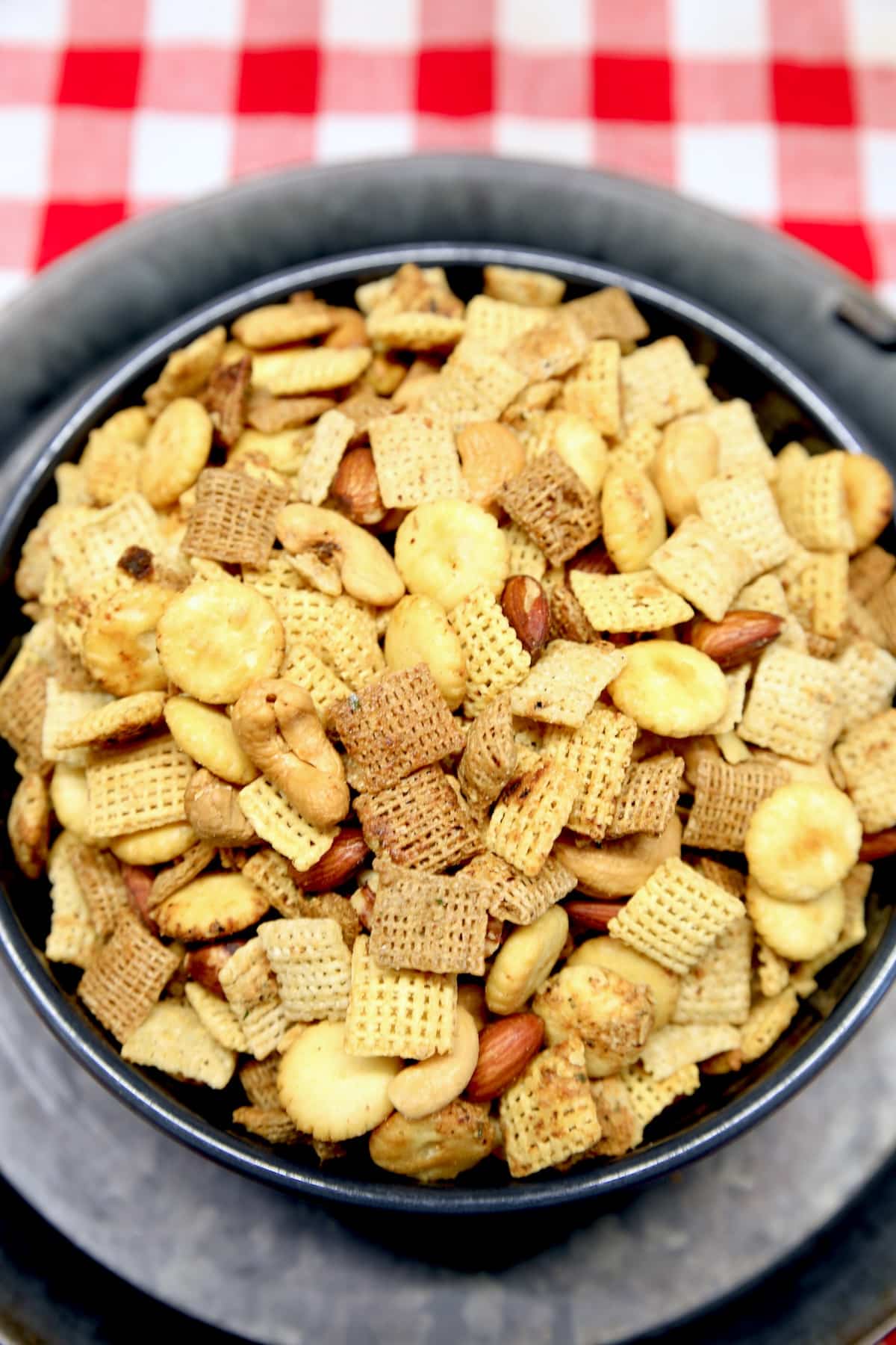 Bowl of chex mix on red check cloth.