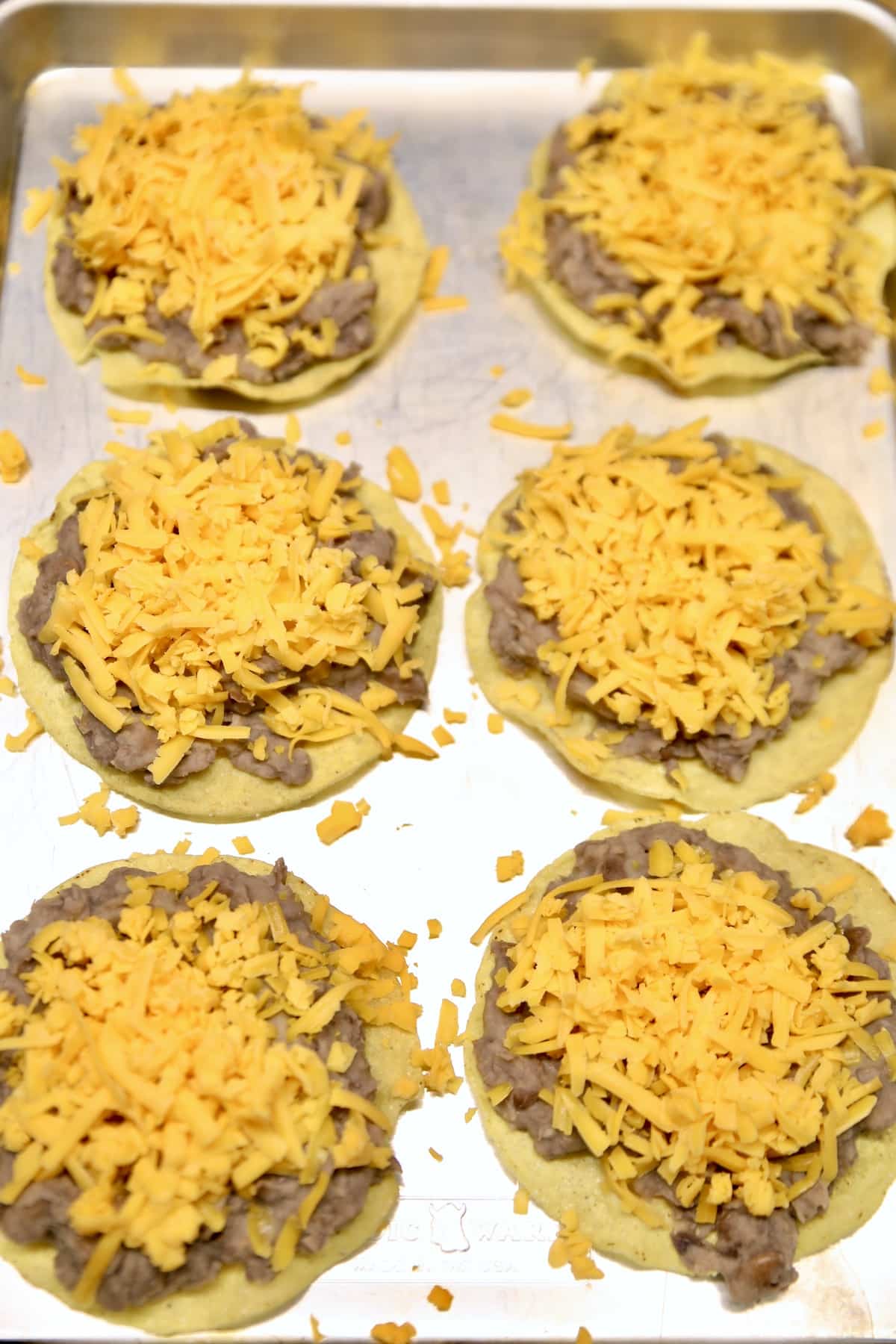 6 Tostadas with refried beans and shredded cheese on a pan.