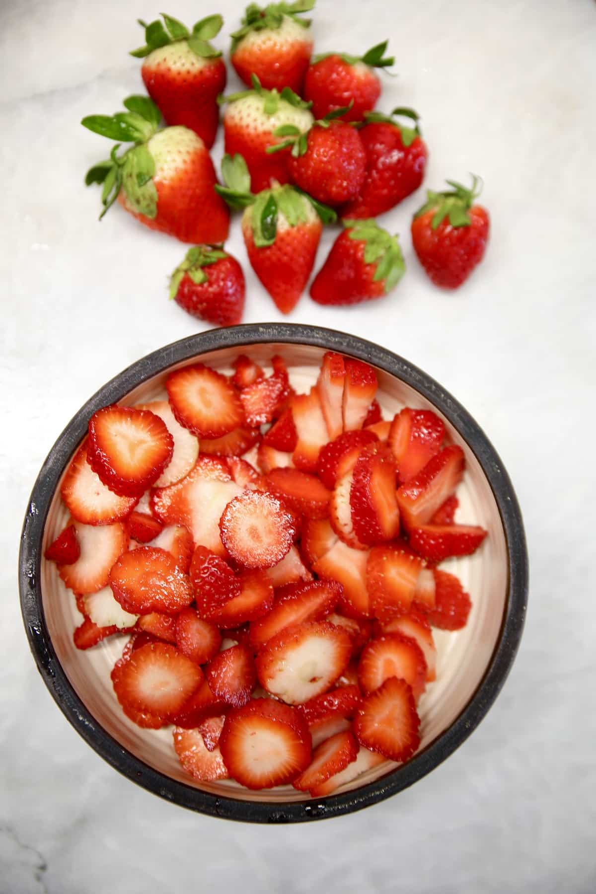 Sliced strawberries in a bowl, whole strawberries next to the bowl.
