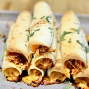 BBQ Chicken Taquitos stacked on a baking sheet.