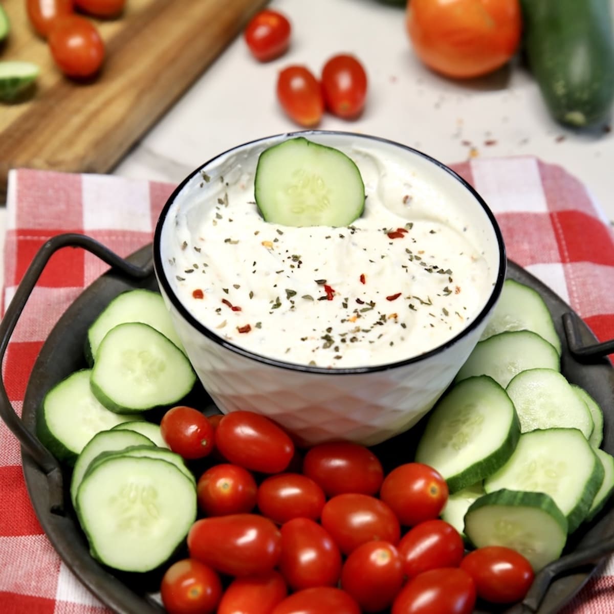Veggie dip in a bowl with cucumber slices and grape tomatoes on a platter.