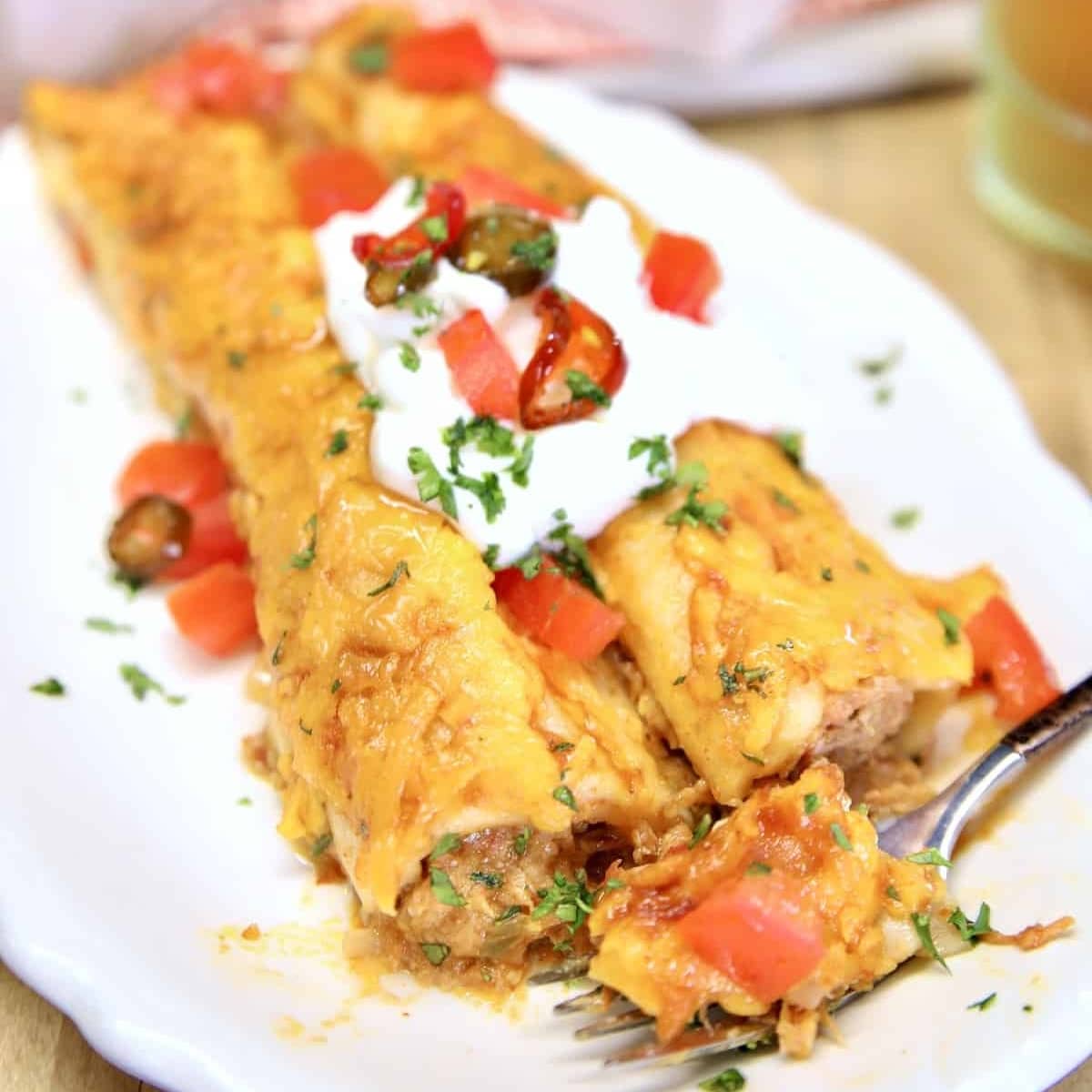 Pulled pork enchiladas on a plate with sour cream and tomatoes.
