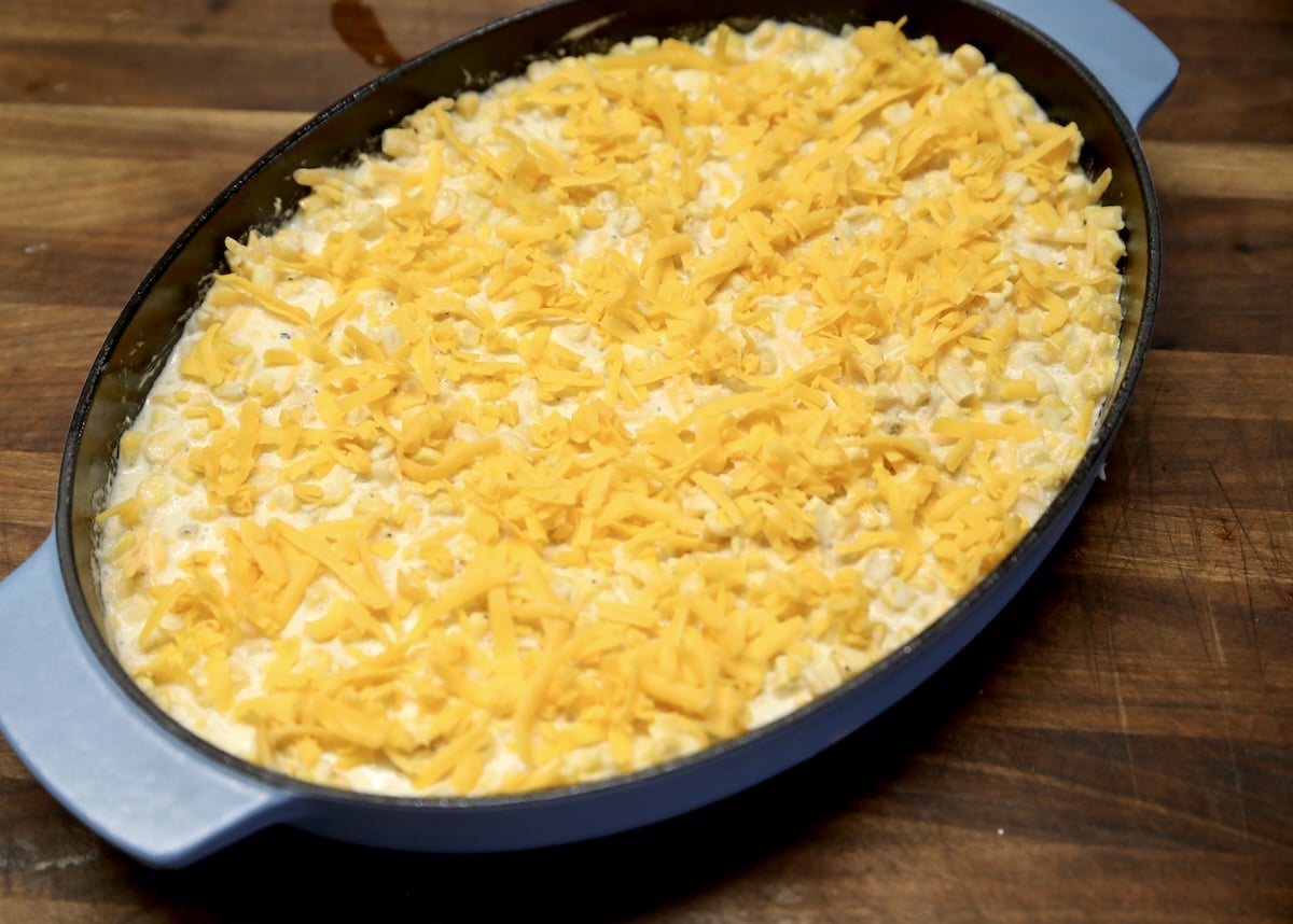 Oval casserole of creamy corn pudding with shredded cheddar.