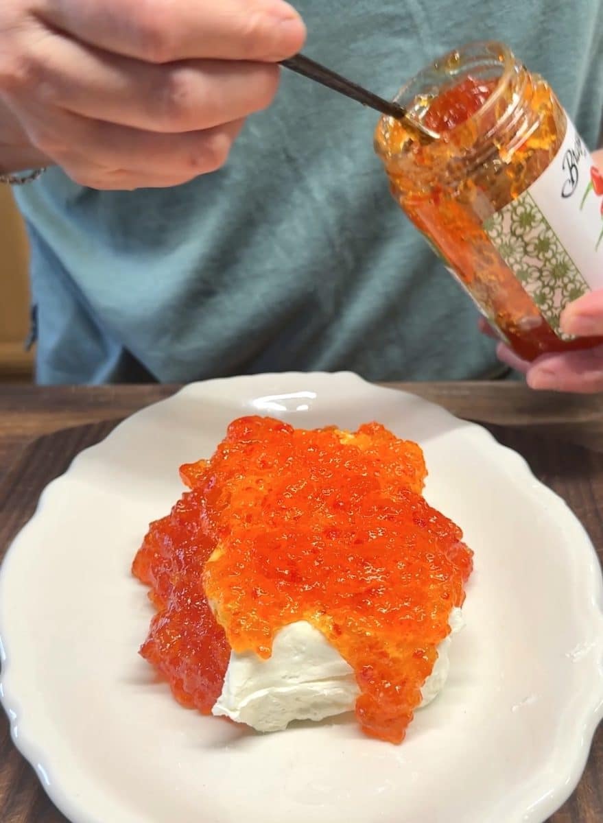 Spooning pepper jelly over cream cheese.