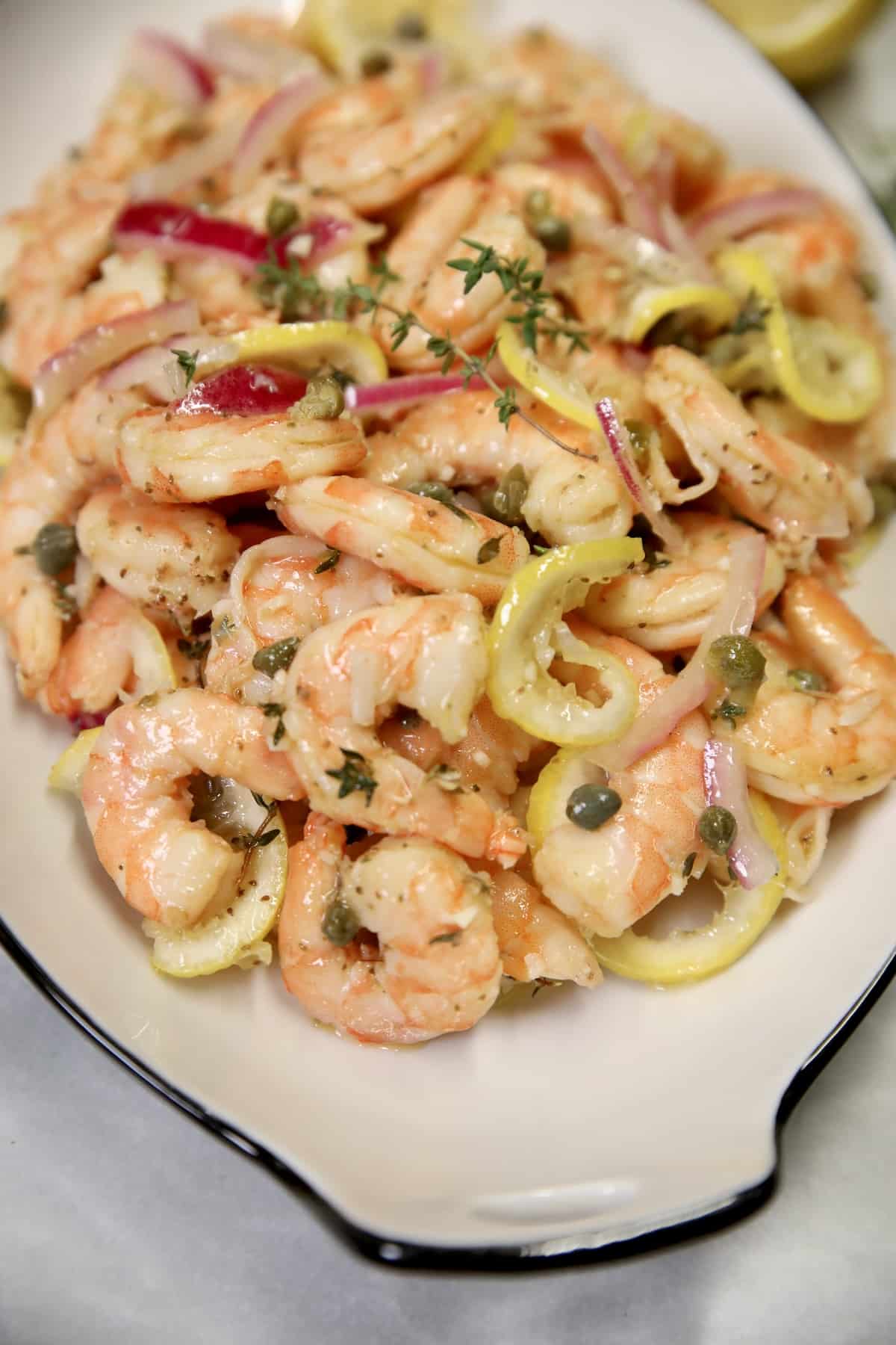 Pickled shrimp on a platter with onion and lemon.