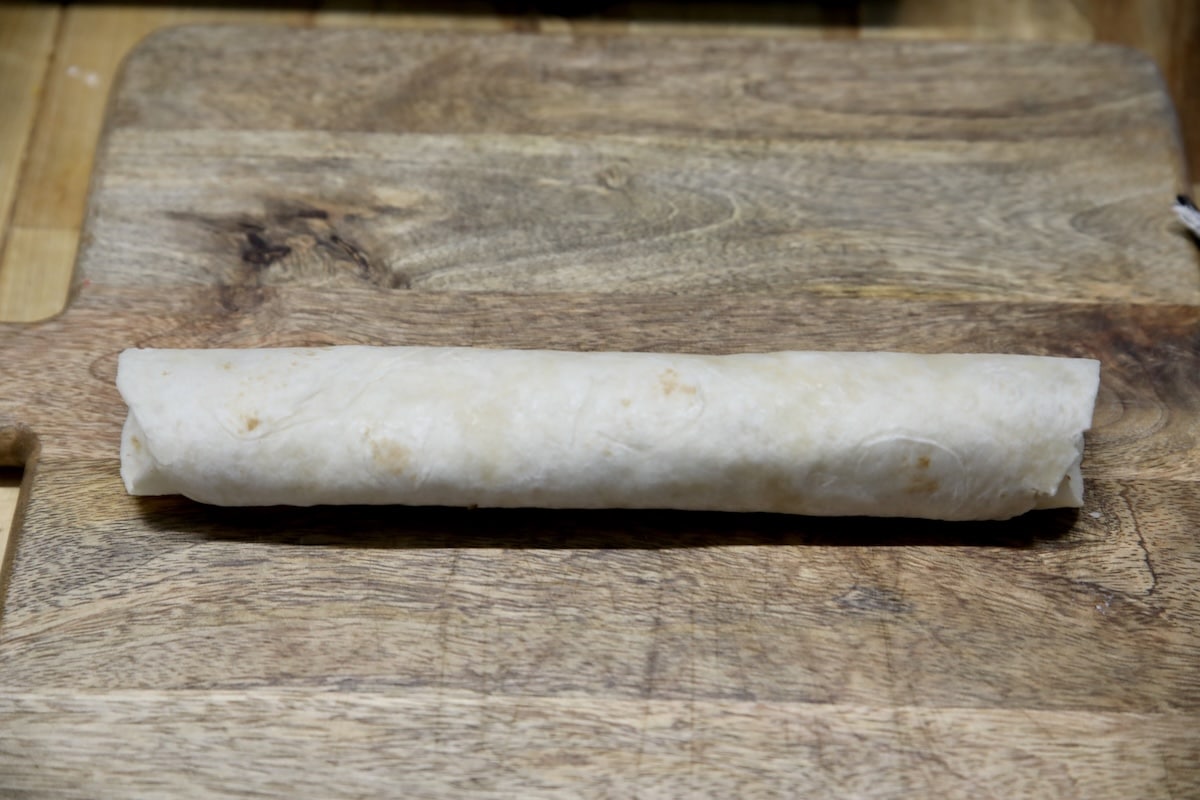 Turkey enchilada rolled up on cutting board.