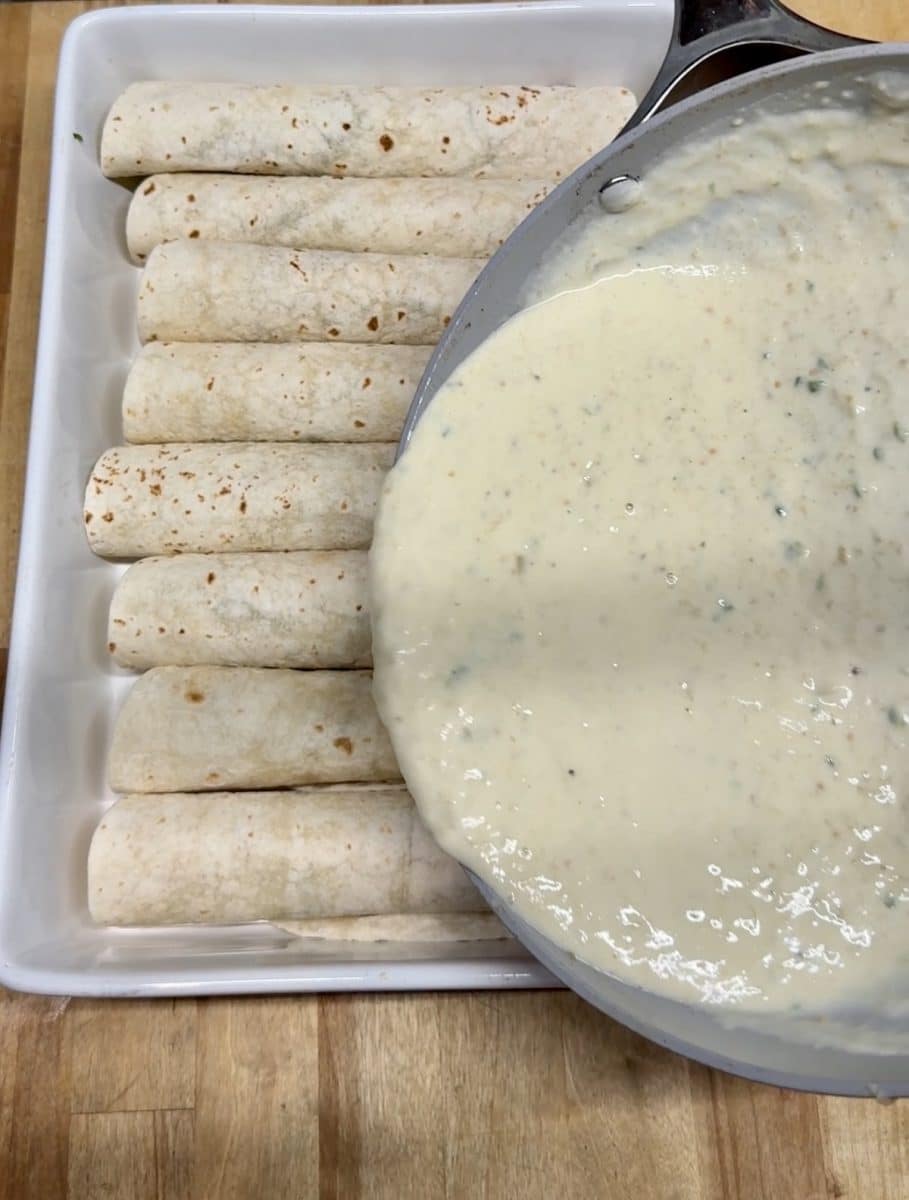 Pouring creamy enchilada sauce over seafood enchiladas.