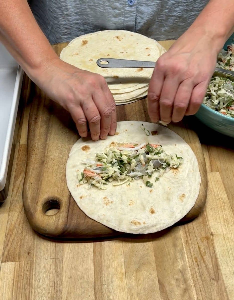 Filling seafood enchiladas in flour tortilla.