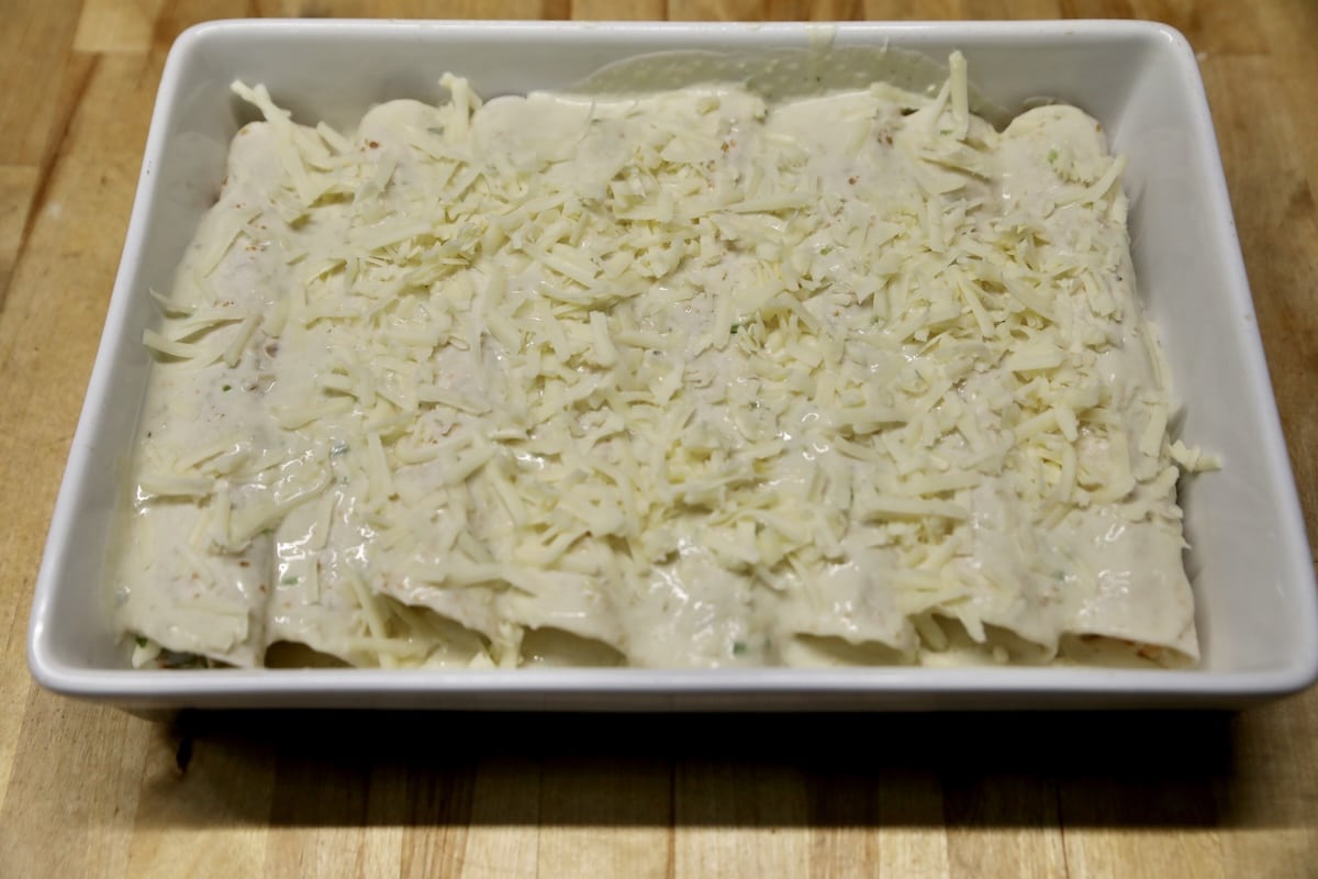 Enchiladas with creamy sauce and shredded cheese ready to bake.