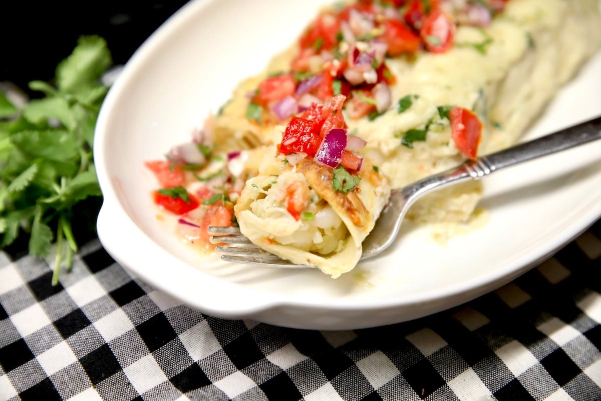 Seafood enchiladas on a plate, fork with bite.