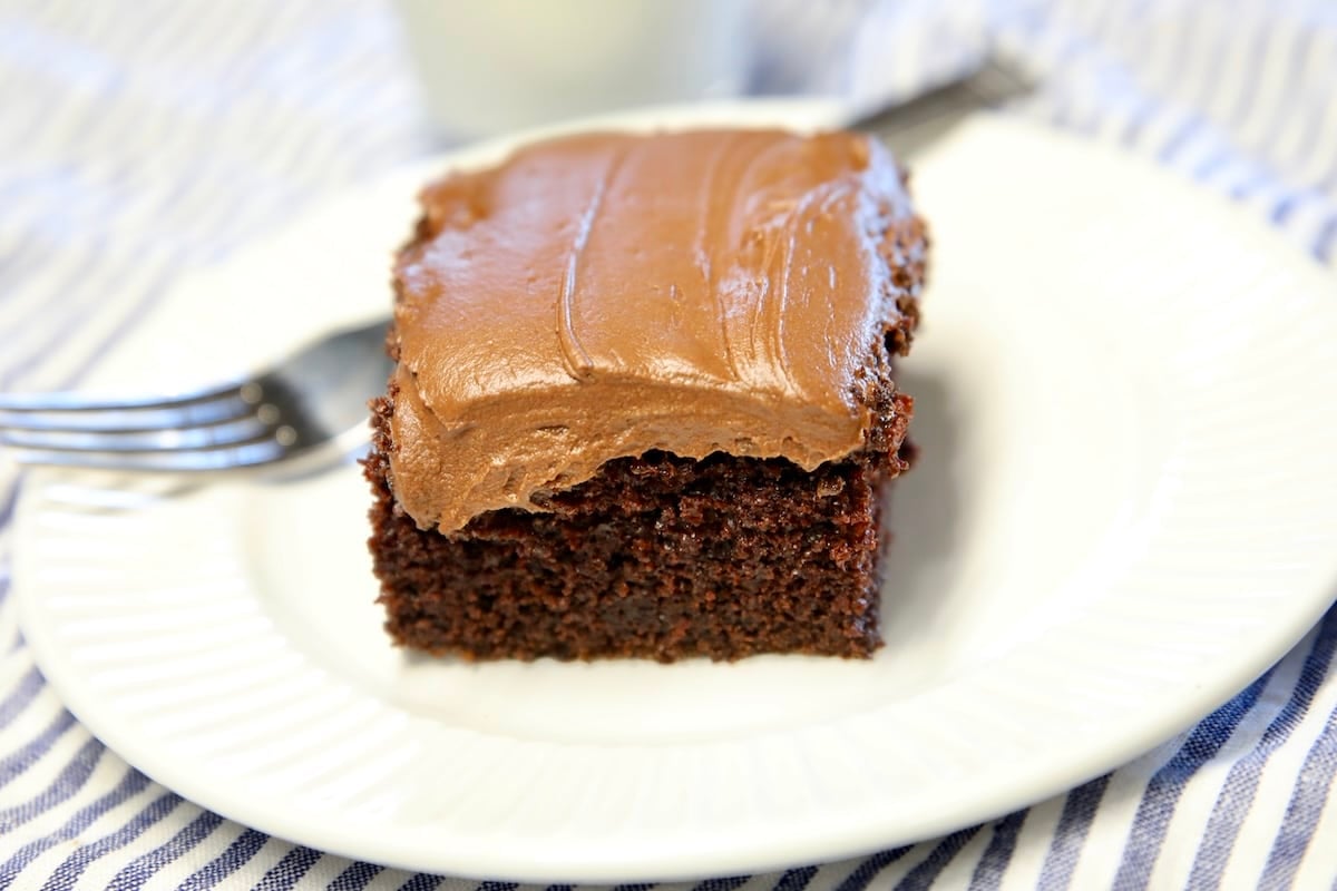 Slice of chocolate cake with frosting, fork on plate.