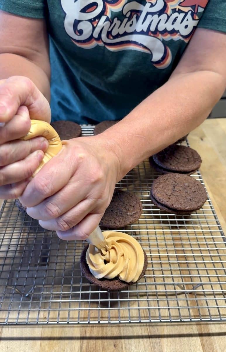 Piping icing onto a cookie for sandwich cookies.