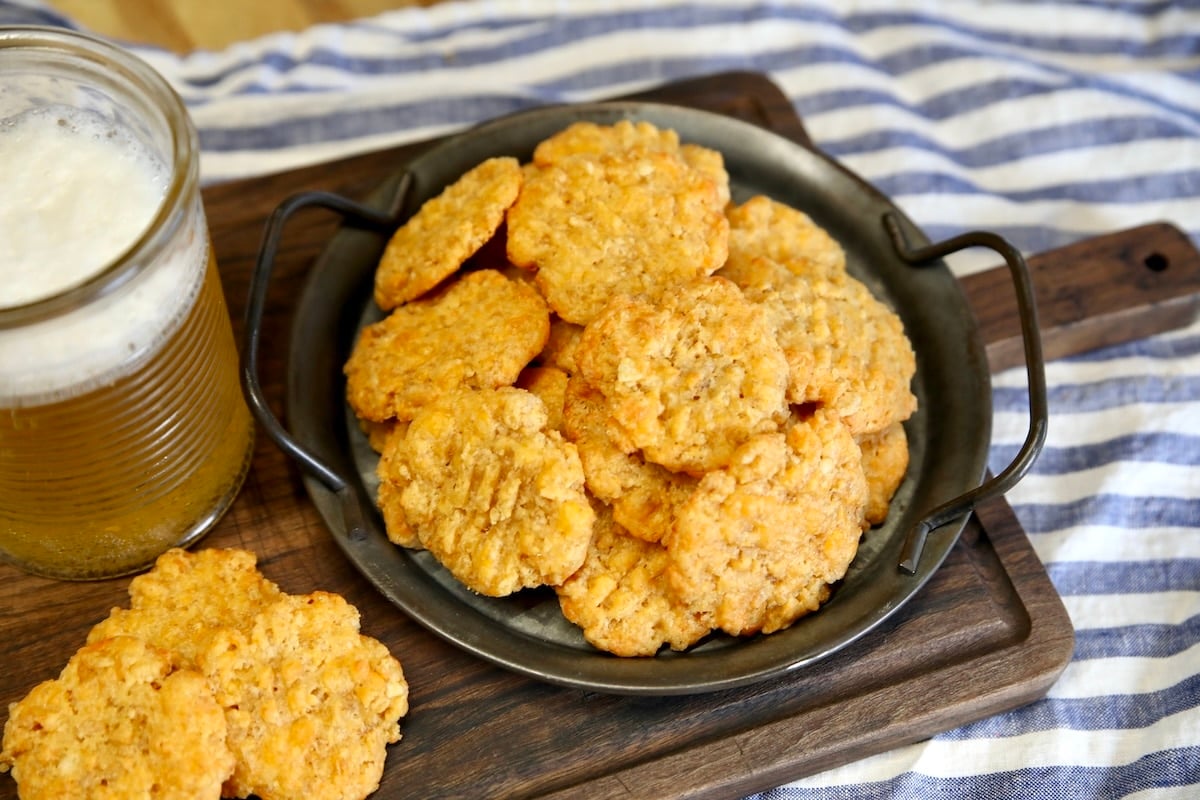 Rice Krispie Cheese Wafers appetizer. Plate of cheese wafers on a cutting board with beer in a glass.