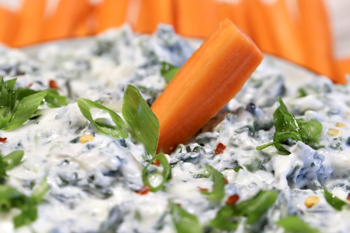 Carrot stick dipping in spinach dip.