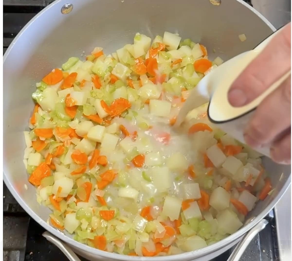 Adding clam juice to vegetables in a pan.