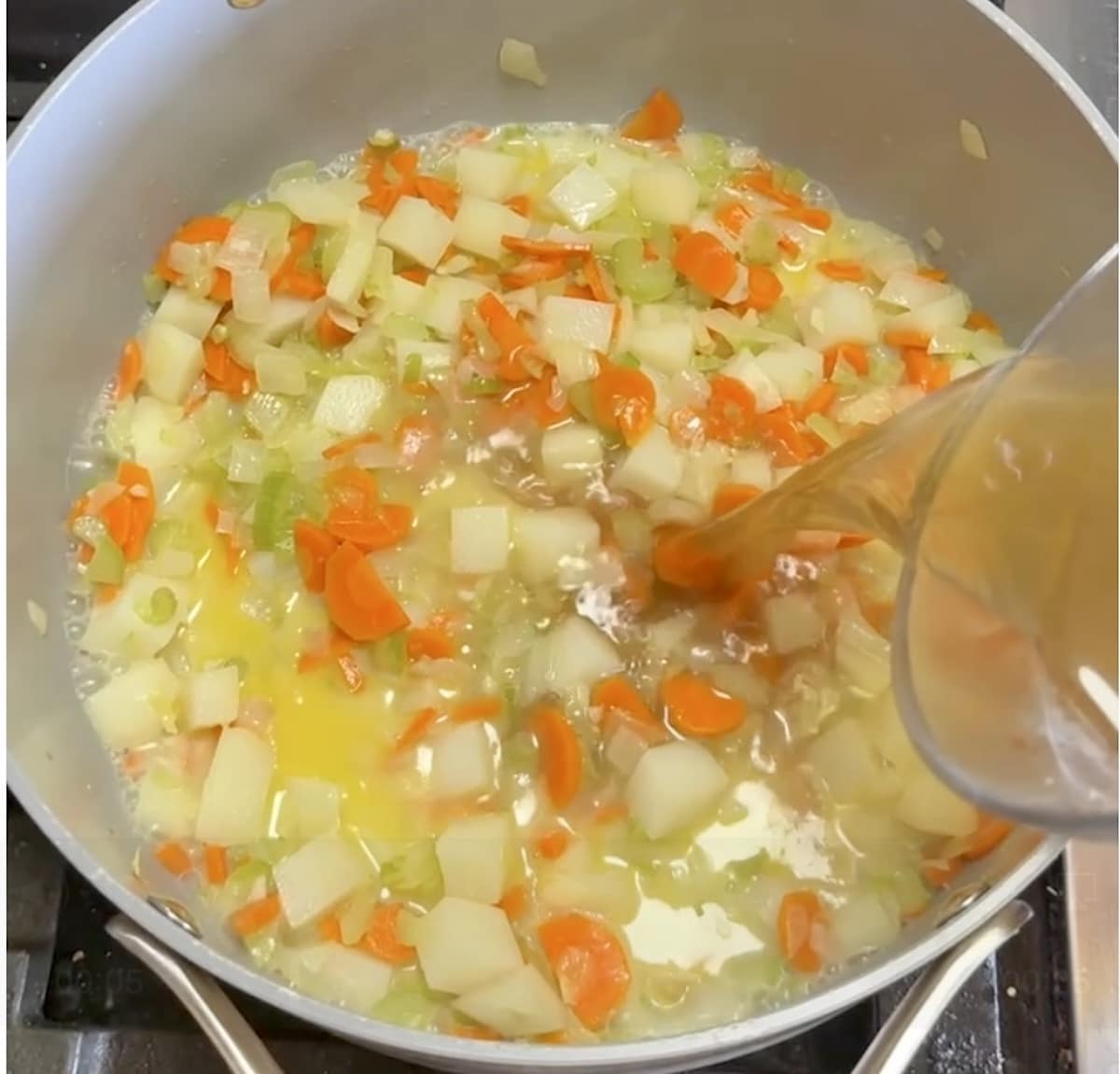 Adding seafood stock to pan of vegetables.
