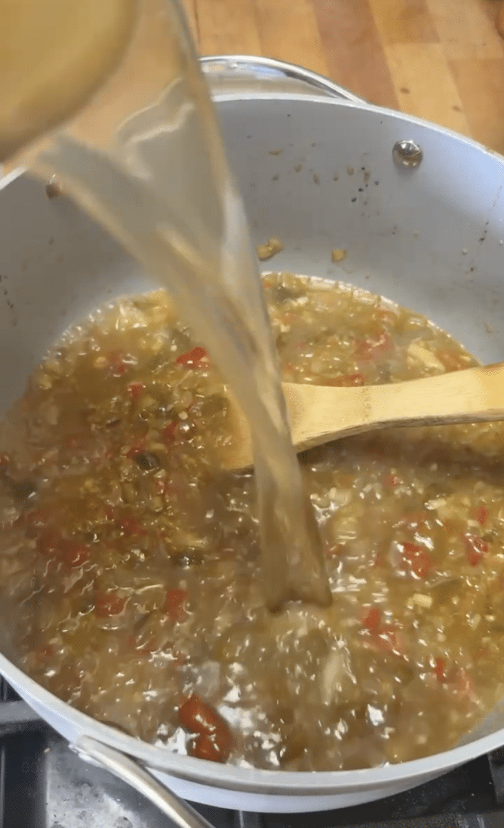 Adding seafood stock to sauteed vegetables for soup.