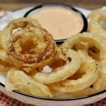 Beer battered onion rings on a platter with sauce.