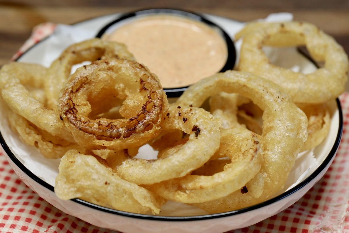 Beer Battered onion rings on a plate with dipping sauce.