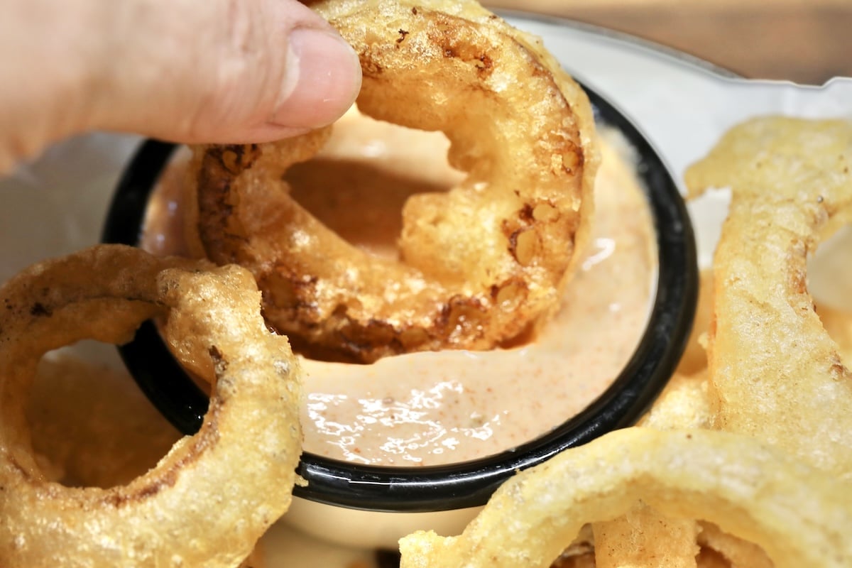 Onion ring dipping into blooming onion sauce.