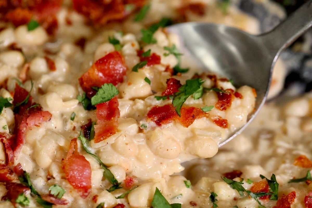Spoonful of white beans with creamy parmesan sauce and crispy bacon. Spoonful of white beans with bacon.