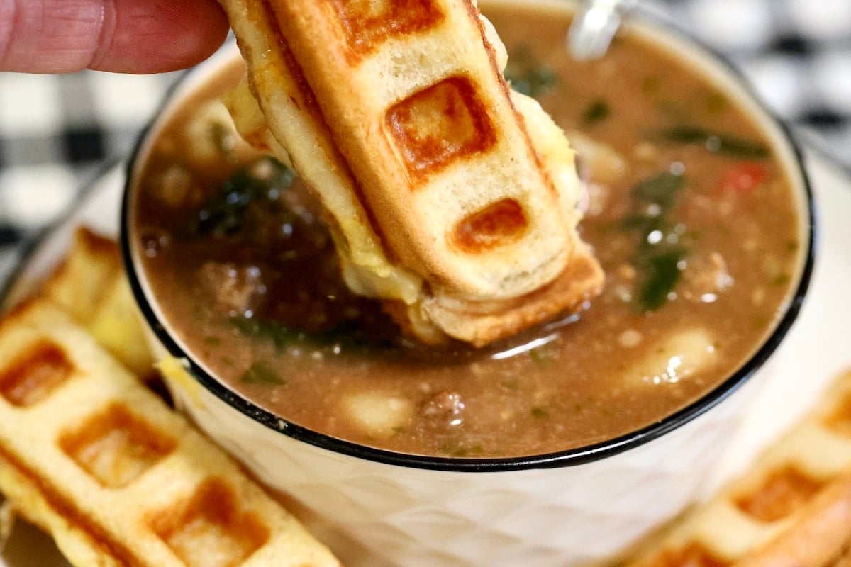 Waffle grilled cheese dunking into bowl of Italian gnocchi soup.