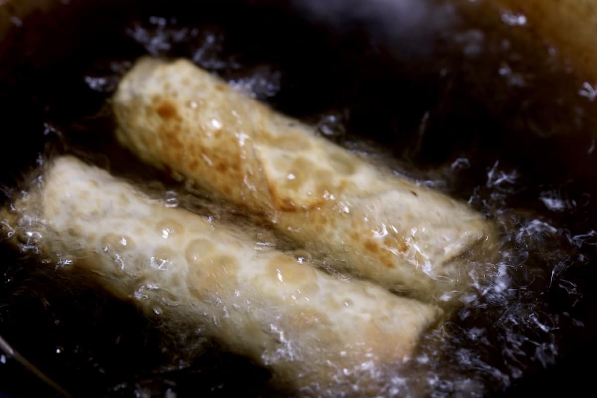 2 egg rolls frying in oil.