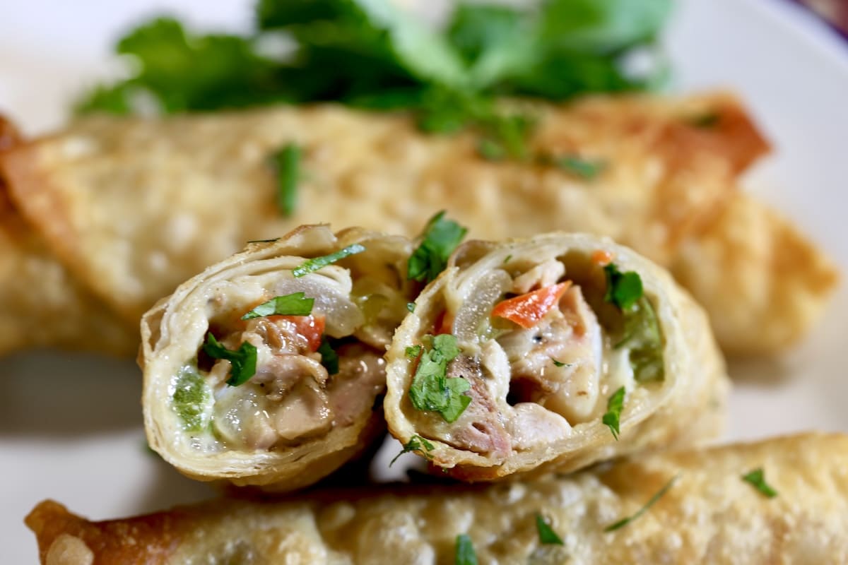 Chicken fajita egg rolls on a plate, cut in half to show filling.