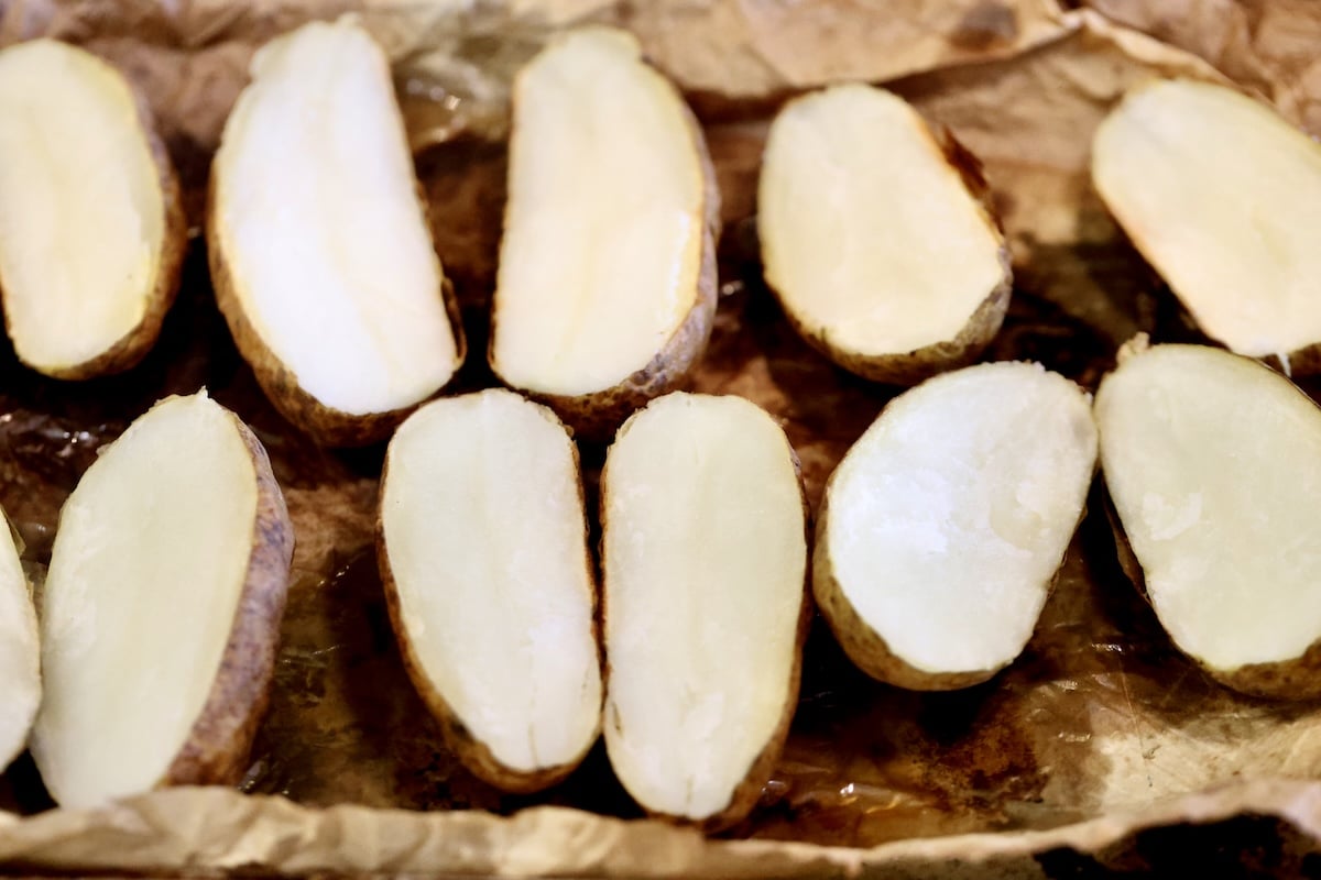 Baking sheet with baked potatoes cut in half.
