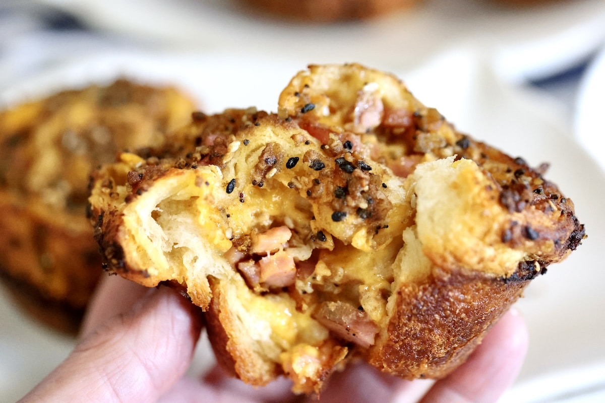 Croissant muffin stuffed with ham and cheddar, opened to show layers.